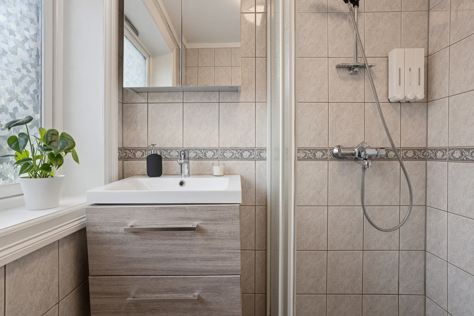 Badet er innredet med dusjhjørne og servant nedfelt i baderomsmøblement. Galleribilde