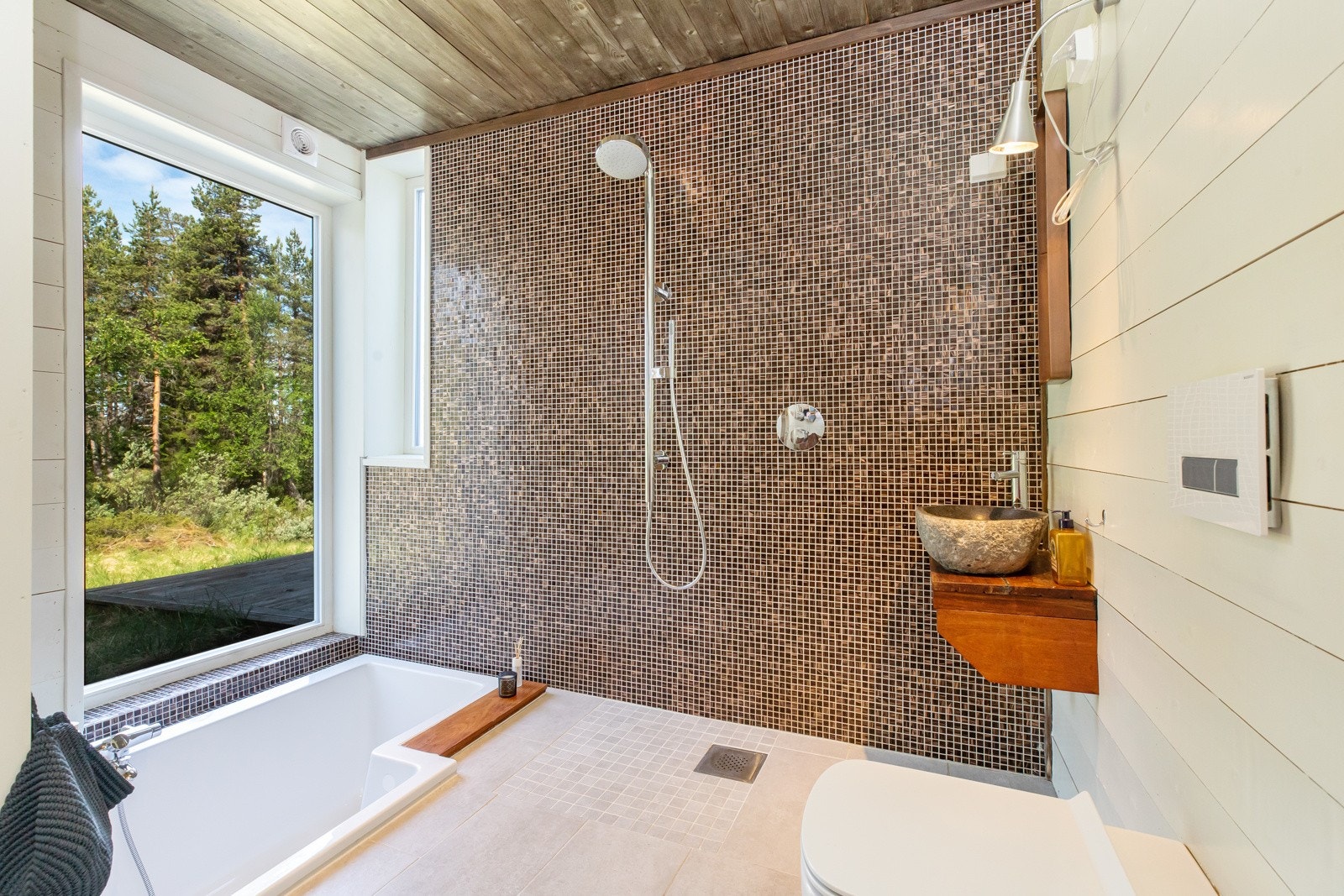 Badet i nyeste delen har lekkert uttrykk med mosaikkfliser på dusjvegg og ellers liggende panel i malt utførelse Galleribilde