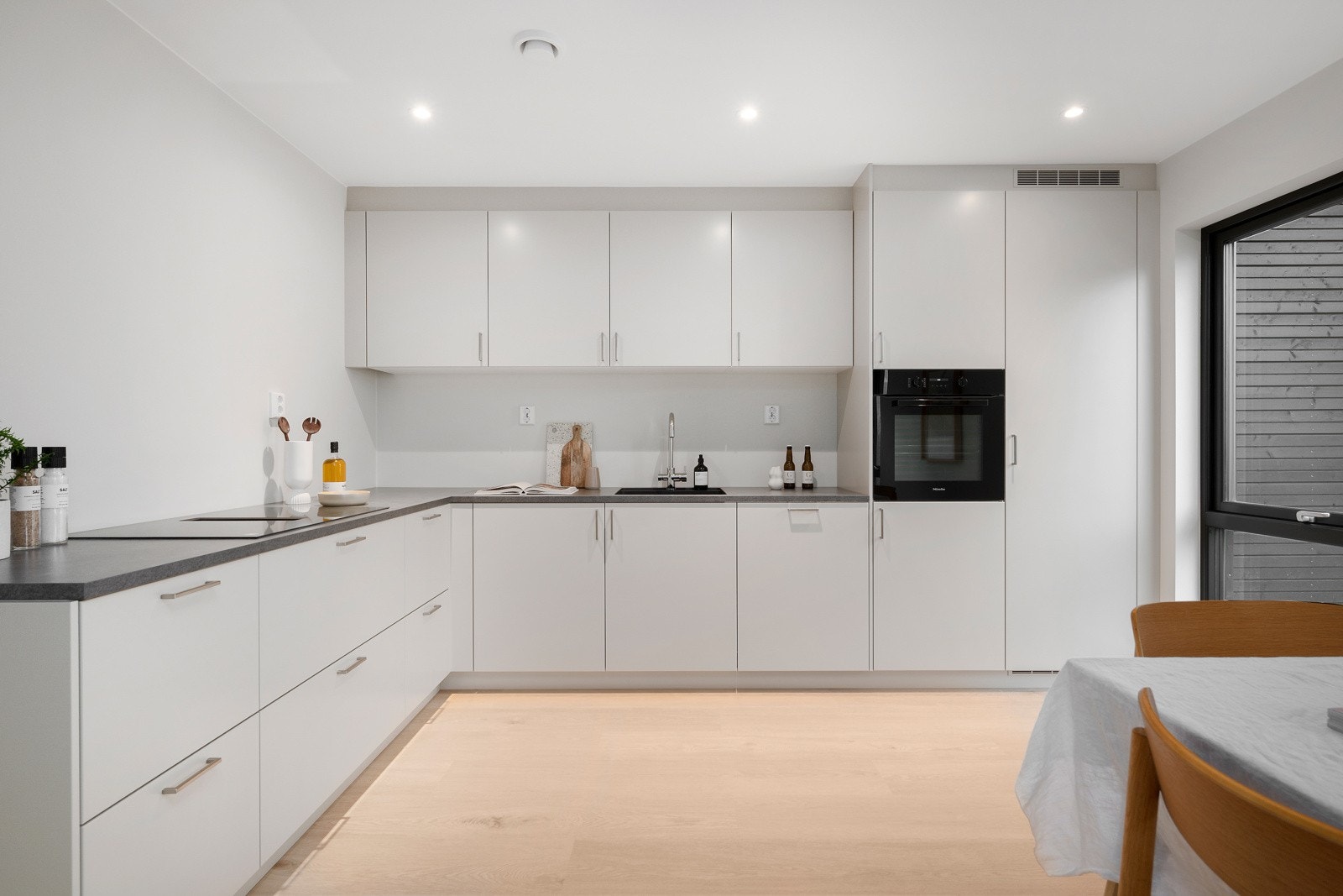 Lyst, moderne og stilrent kjøkken i egen sone med store vindusløsninger i to himmelretninger som gir rikelig med dagslys. Galleribilde