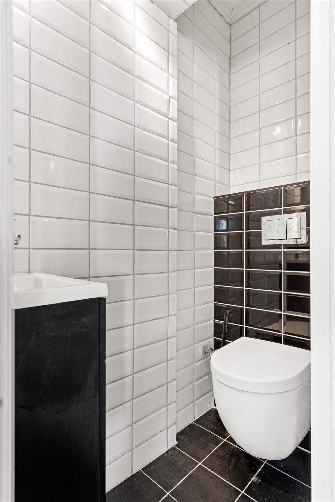 Toalettrom med fliser på gulv og vegger, utstyrt med veggmontert wc og servantskap. Galleribilde