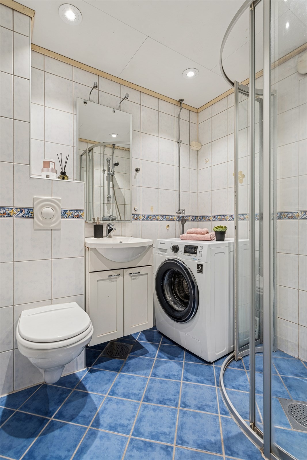 Badet har flislagt gulv med elektriske varmekabler og fliser på veggene. Rommet er innredet med en servant nedfelt i baderomsinnredning, et veggmontert toalett, dusjhjørne med dusjvegger og opplegg for vaskemaskin. Galleribilde