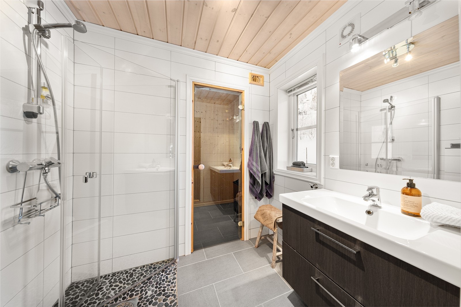 Badet har inngang til badstue. Badet har elektriske varmekabler. Det er innredet med servantinnredning med speil, veggmontert toalett og hjørnedusj med glassdører. Galleribilde