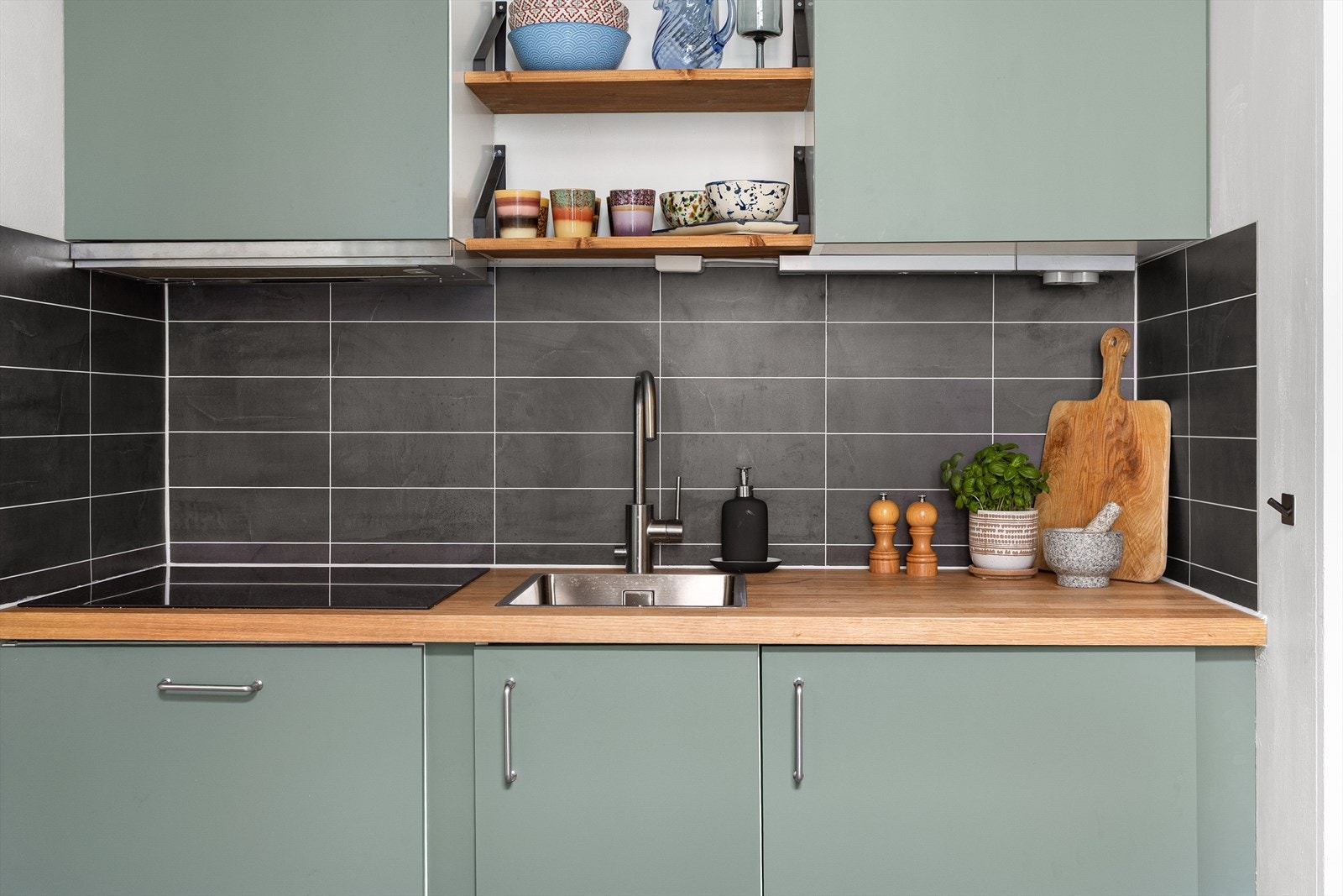 Moderne kjøkkeninnredning med glatte fronter, benkeplate av tre, integrert induksjonstopp og kjøleskap. Galleribilde