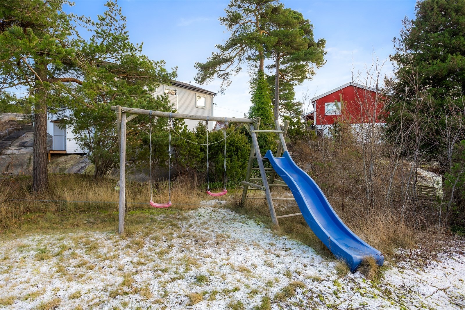 Skrående tomt med gressplen og beplantninger. Asfaltert innkjørsel og belegningsstein foran garasje. Galleribilde