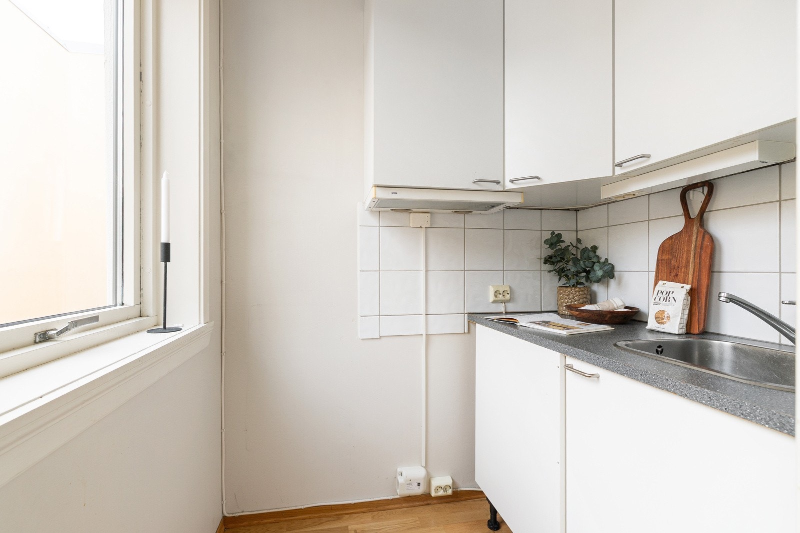 Eldre kjøkkeninnredning med hvite glatte fronter, nedfelt vaskekum i børstet stål med ettgreps krummet armatur Galleribilde