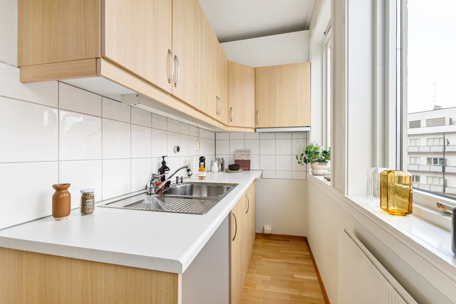 Kjøkken i delvis åpen løsning. Tvis-kjøkkeninnredning med glatte plastlaminerte fronter med imitasjon av finér. Innredning med mekanisk avtrekksvifte over stekesonen og opplegg for oppvaskmaskin og komfyr Galleribilde