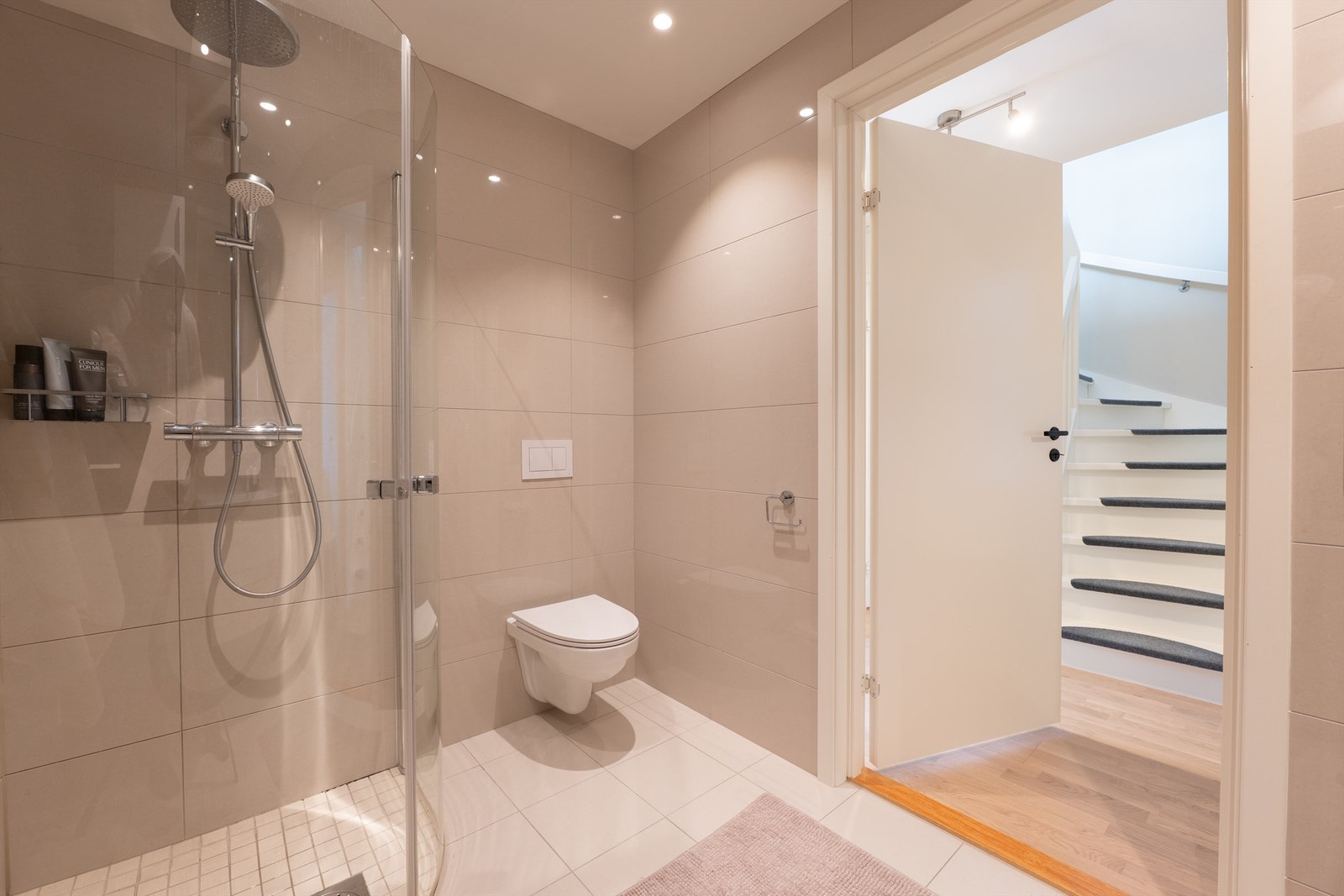 Dusjdørene kan svinges inn for å maksimere tilgjengeligheten av badets ca. 5 kvm. Gulv og vegger er flislagt, i gulvet er det også elektrisk varme. Galleribilde