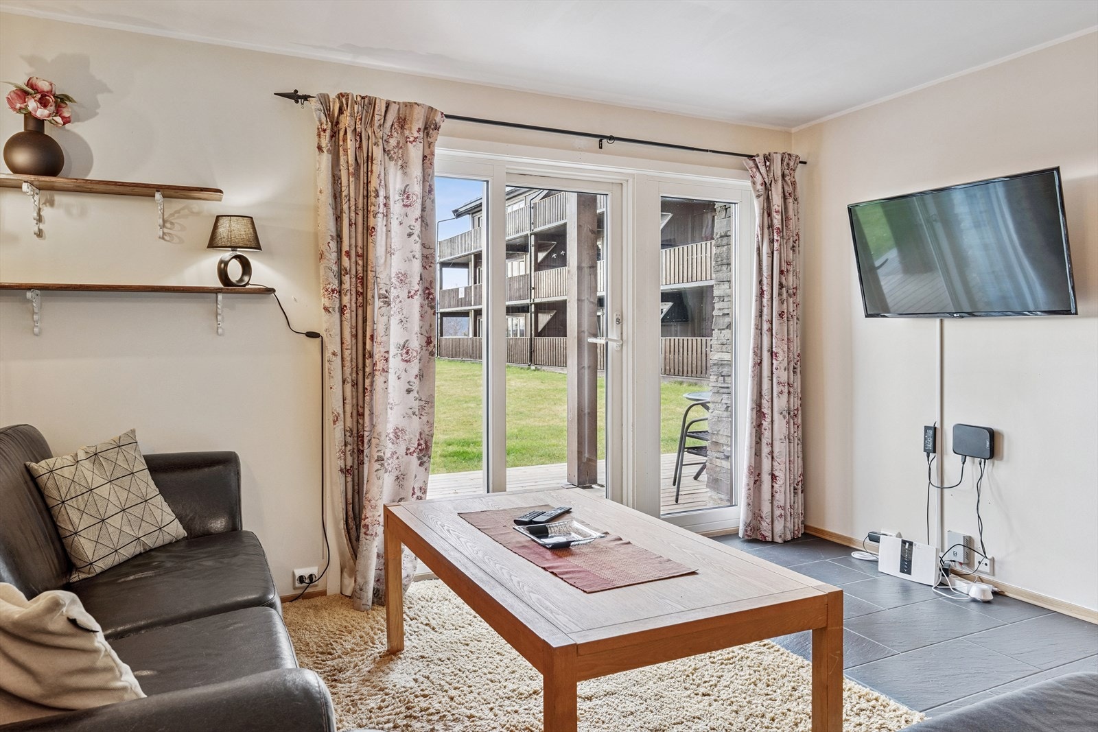 En dobbel terrassedør fører ut til en liten terrasse som er delvis overbygd. Galleribilde