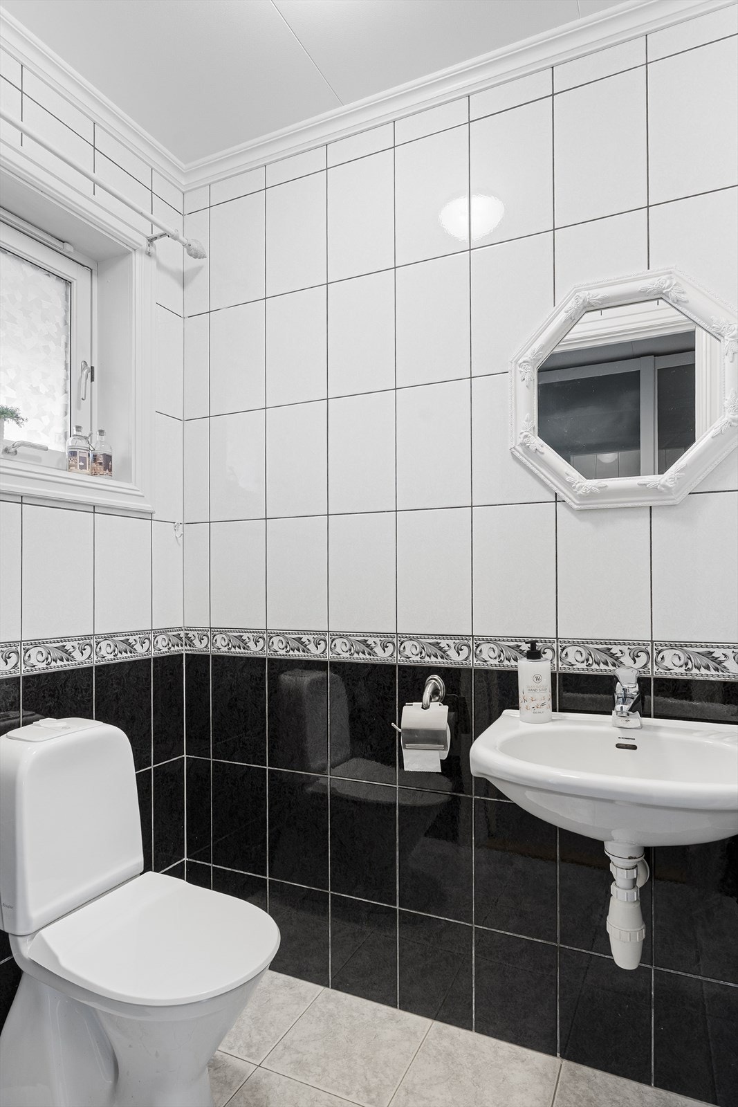 Toalettrom i 1. etasje med fliser på gulv og vegger - rommet er innredet med gulvstående toalett og vegghengt servant Galleribilde