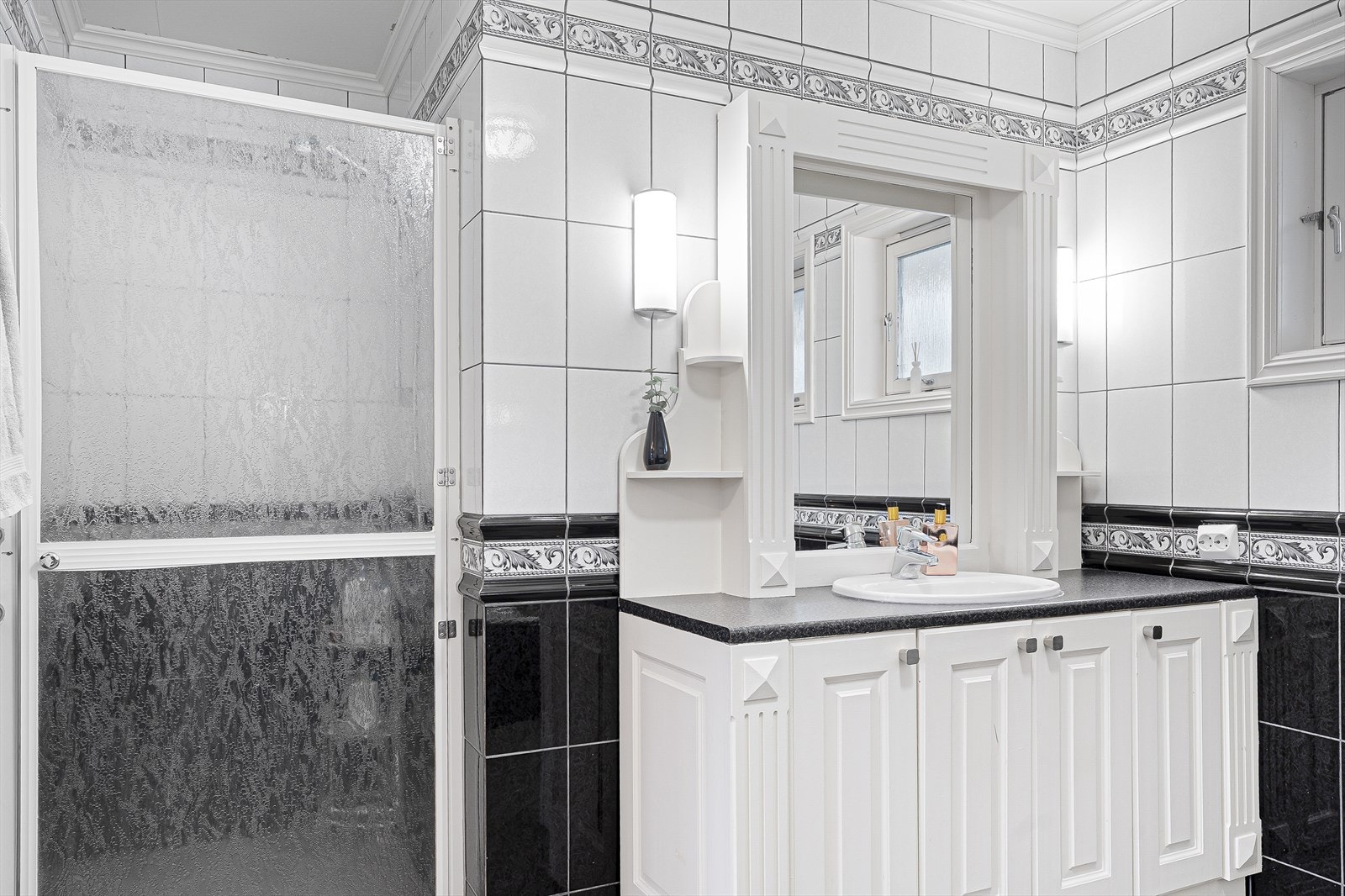 Badet har hvit baderomsinnredning, gulvstående toalett, innebygd badekar og stedbygd dusj med dusjdør Galleribilde