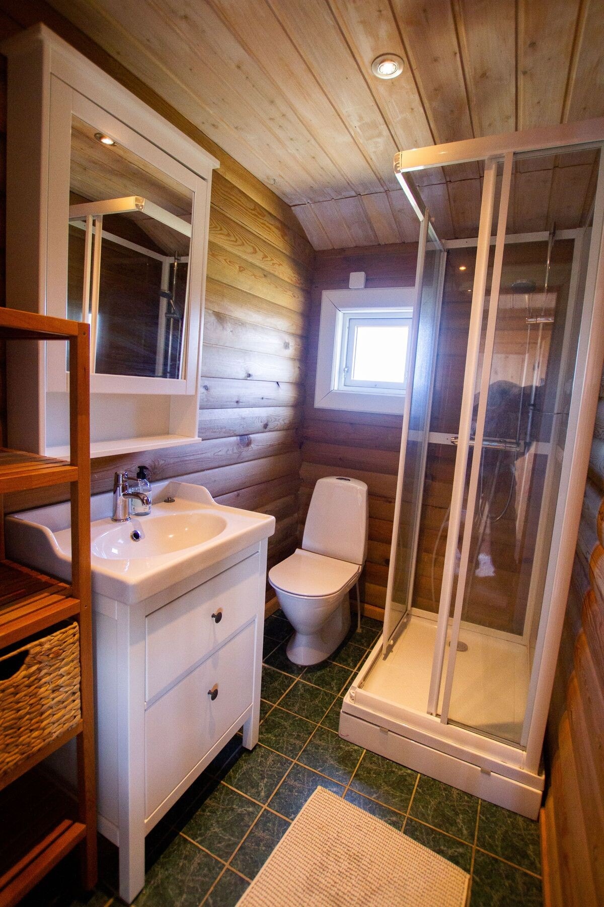 Bad har flislagt gulv med varme og vegger kledd med trepanel. Servantinnredning, toalett og dusjkabinett. Galleribilde