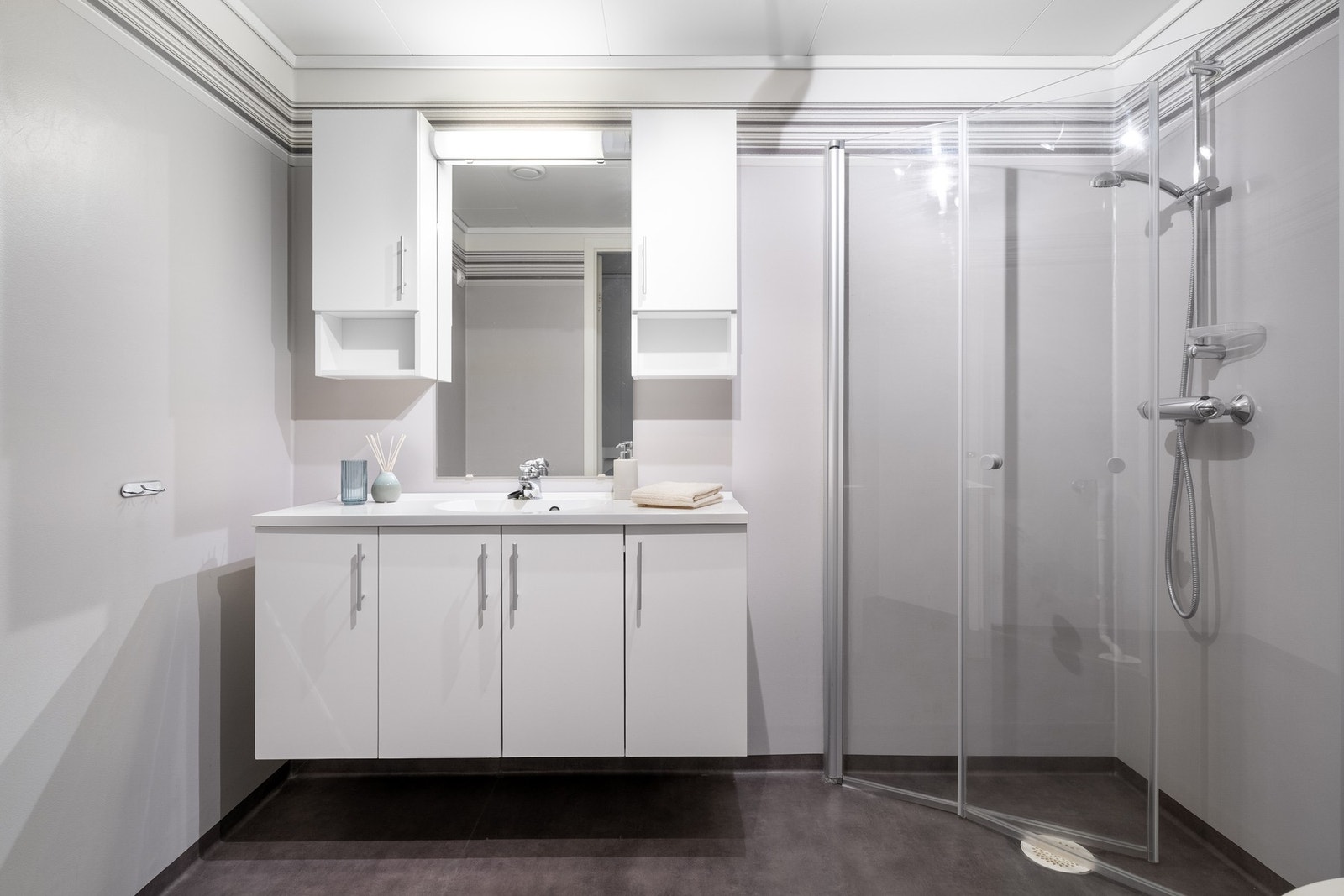 Badet har vinylbelegg på gulv og vegger. Badet er innredet med servant på skuffeseksjon og speil. Galleribilde