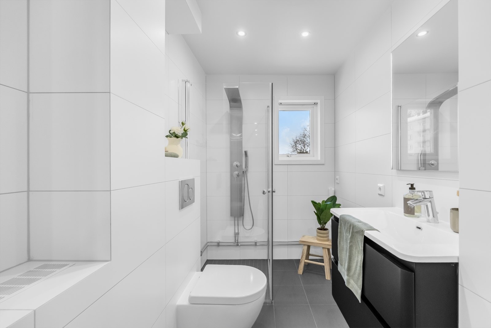 Badet er helfliset med store, hvite veggfliser og mørkere gulvfliser. Galleribilde