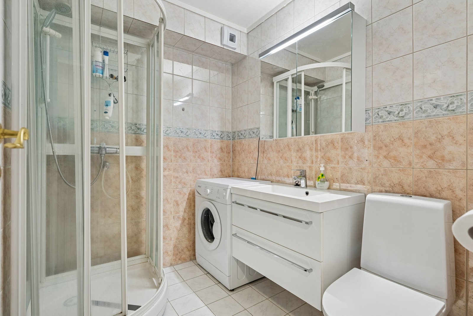 Flislagt bad med elektriske varmekabler i gulvet. Badet er innredet med dusjkabinett, baderomsinnredning med heldekkende servant, toalett og opplegg for vaskemaskin. Galleribilde