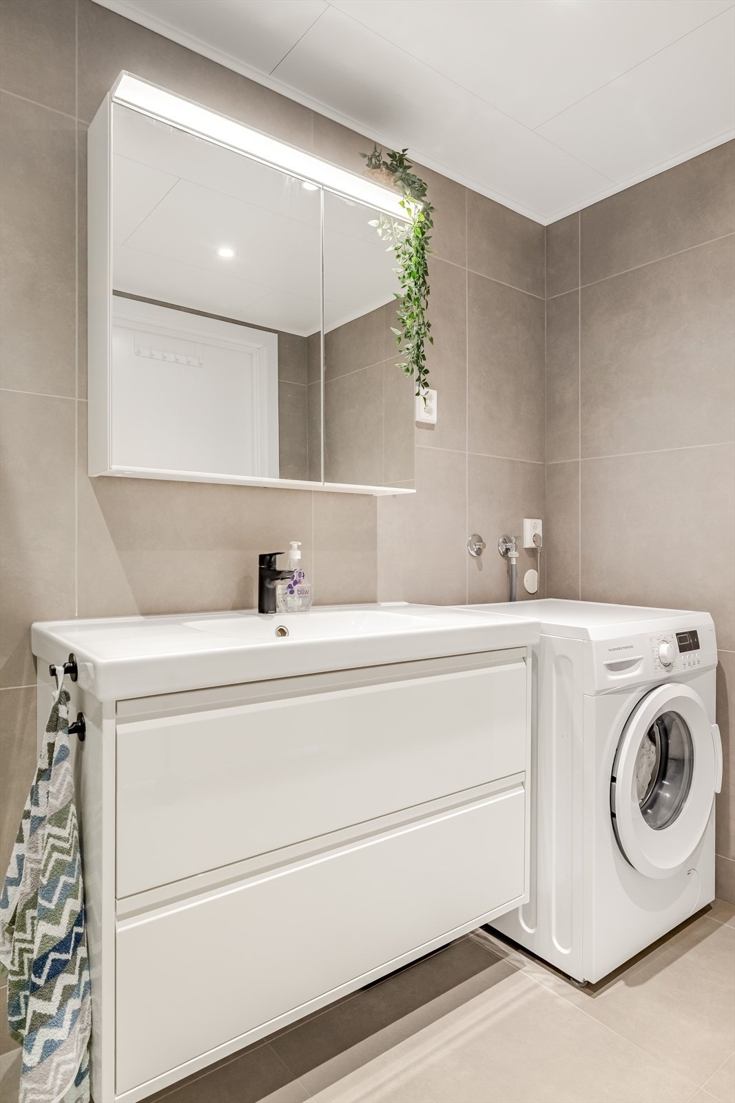 Baderomsinnredning med skuffer og heldekkende servant. I overkant av servanten er det speilskap og overlys. Det er opplegg for vaskemaskin på badet. Galleribilde