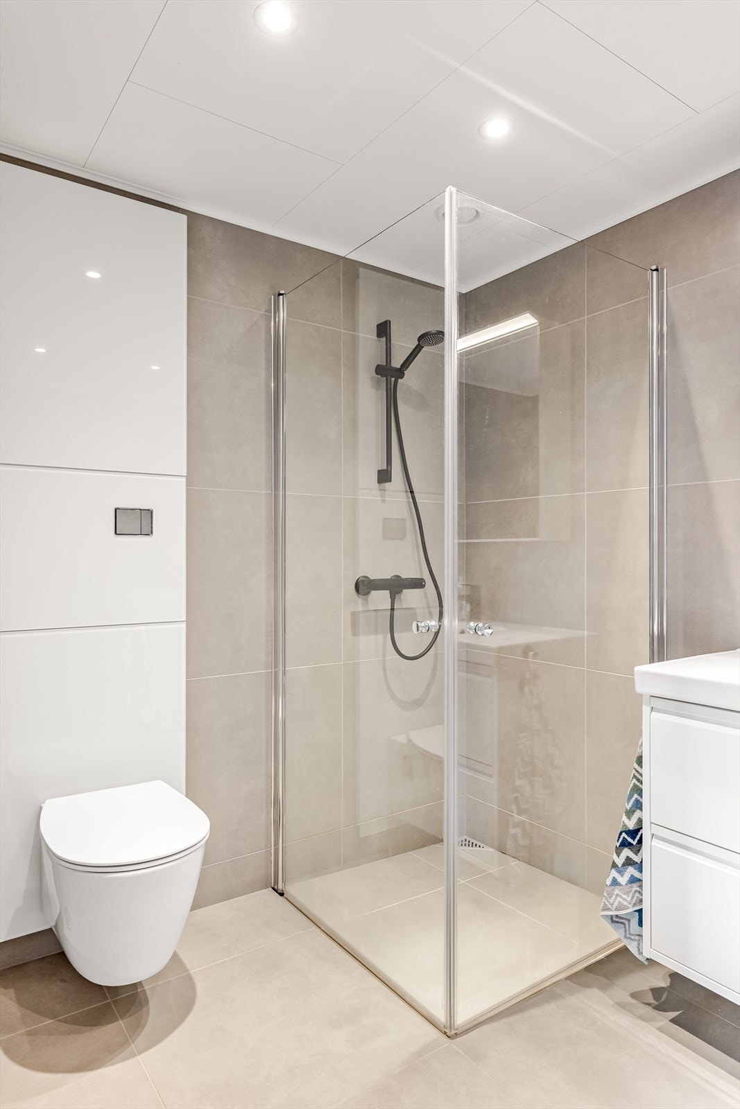 Dusjhjørne med innfellbare dusjdører og vegghengt dusjarmatur gir et stilrent uttrykk. Vegghengt toalett. Galleribilde