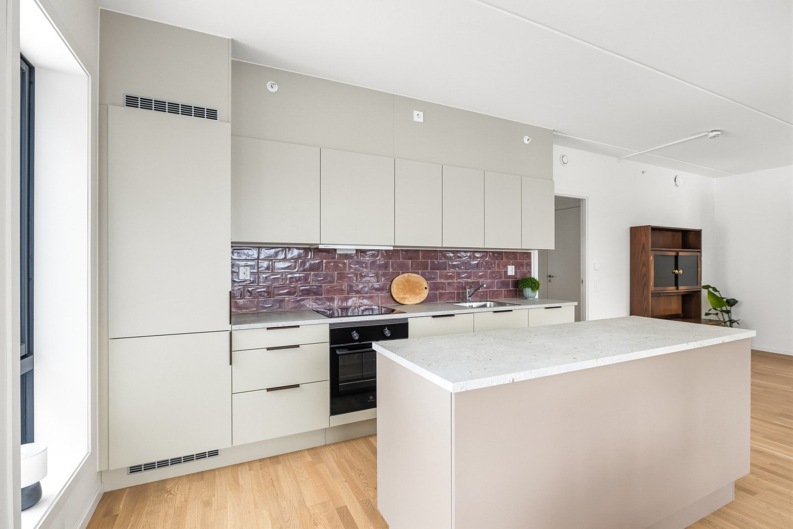 Den åpen løsningen mellom stue og kjøkken er adskilt med en stor og romslig kjøkkenøy. Øyen gir god arbeidflate og blir et sosialt midtpunkt mellom kjøkkenet, stuen og spiseplassen. Galleribilde