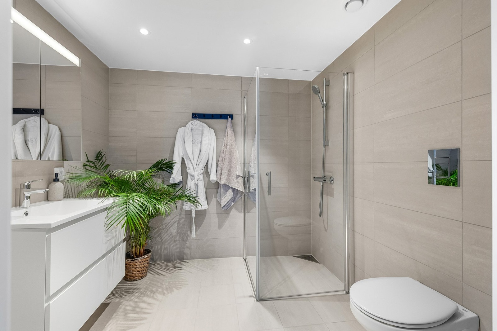 Baderommet er utstyrt med vegghengt servantskap med skuffer og overliggende servant med ett-greps armatur, vegghengt toalett og opplegg for vaskemaskin og tørketrommel. Galleribilde