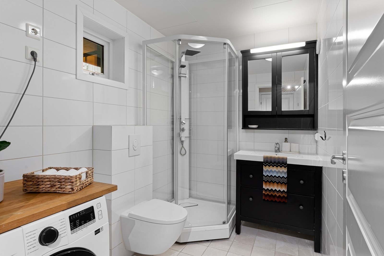 Kjekt bad med fliser på vegger og gulv. Innredet med badromsinnredning, vegghengt toalett, dusjkabinett og opplegg/plass for vaskemaskin og kondenstørketrommel. Galleribilde