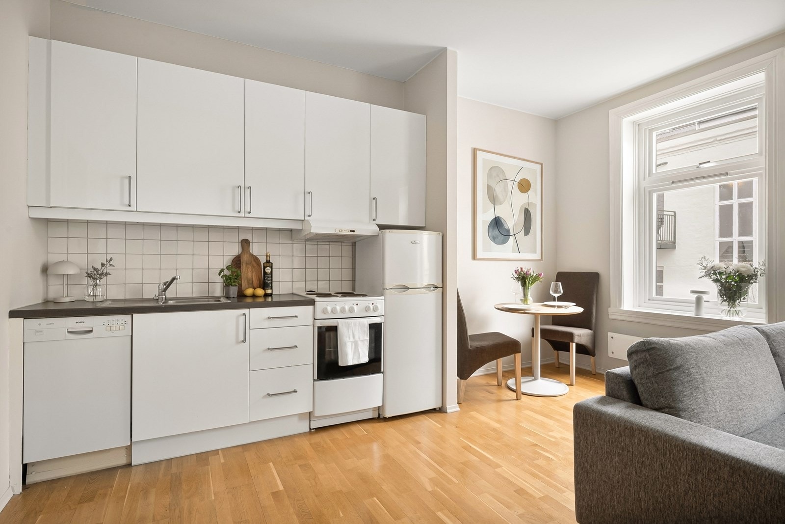 Stilrent kjøkken med glatte fronter. Laminat benkeplate med nedfelt vask og kullfilterventilator over kokeplass. Det er frittstående hvitevarer. Galleribilde