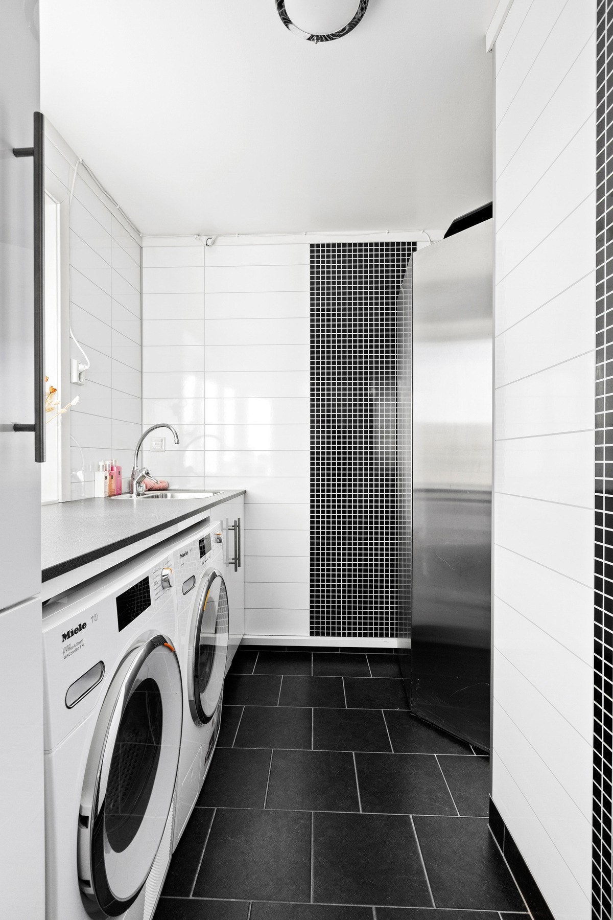 Praktisk vaskerom innredet med benkeskap, utslagsvask og opplegg for vaskemaskin. Galleribilde