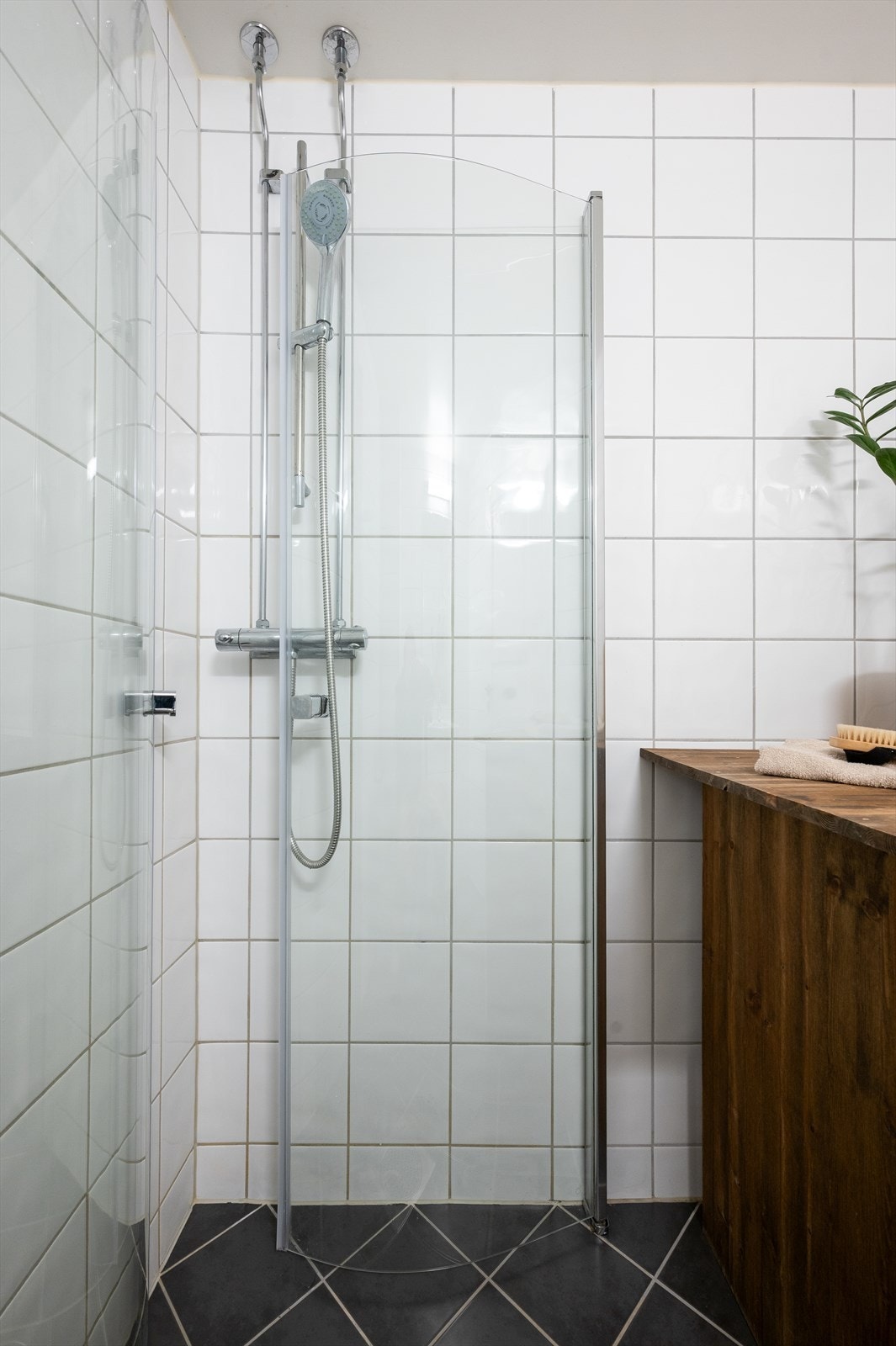 Badet inneholder gulvstående toalett, servant på vegghengt servantskap med speil og lys over. Dusjhjørne med vegghengte dursjører. Galleribilde