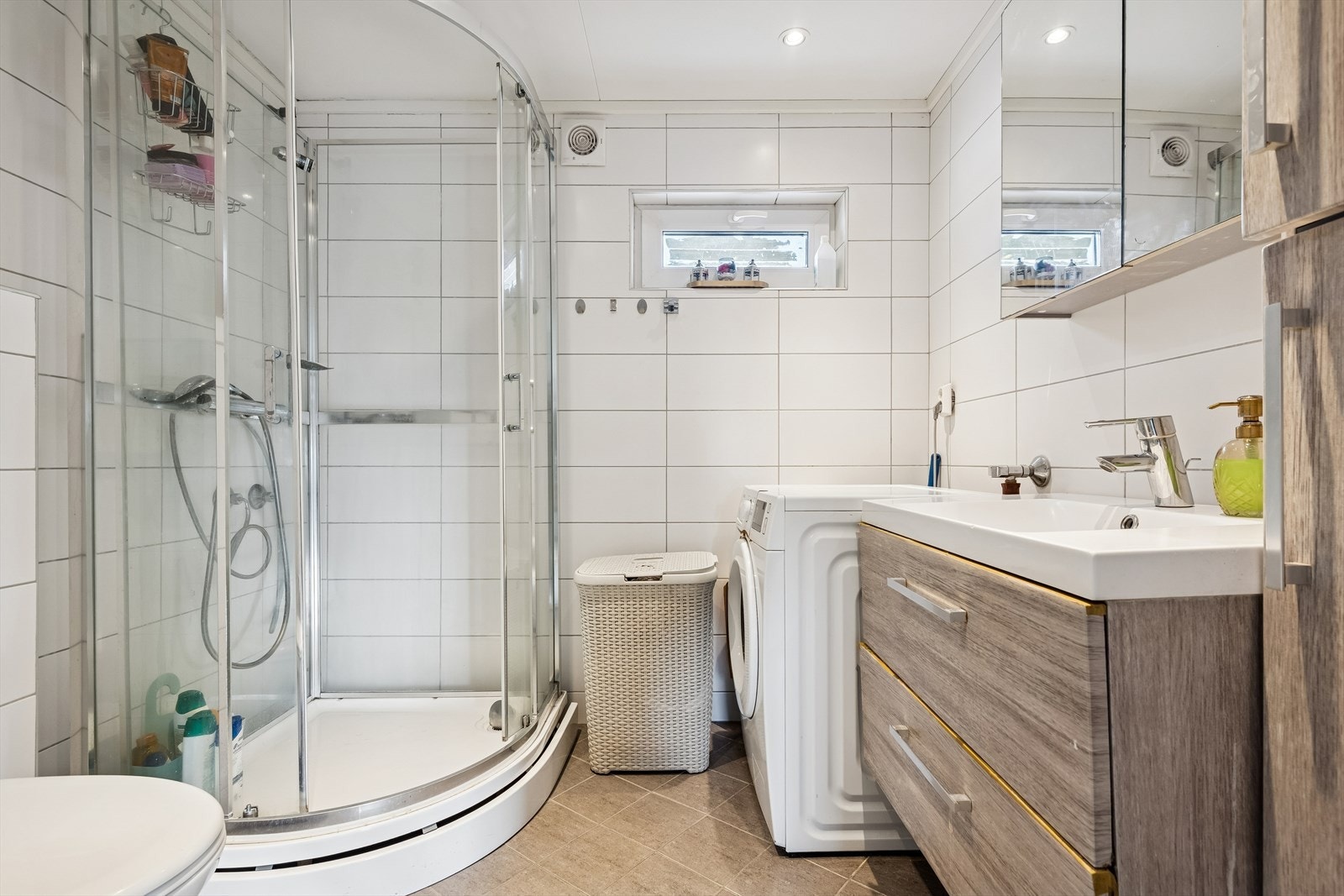 Flislagt bad med dusjkabinett, servantinnredning og opplegg for vaskemaskin. Galleribilde