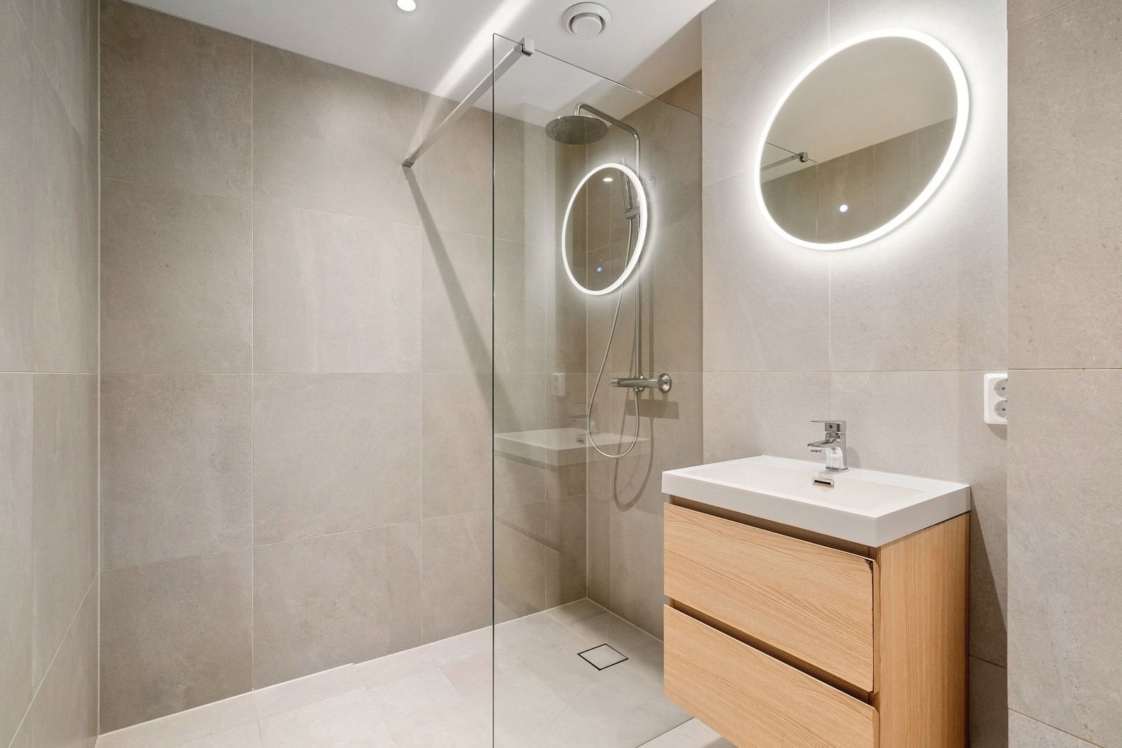 Badet er innredet med nedsenket dusjnisje med skillevegg i herdet glass, vegghengt toalett, servantseksjon med skuffer og speil. Galleribilde