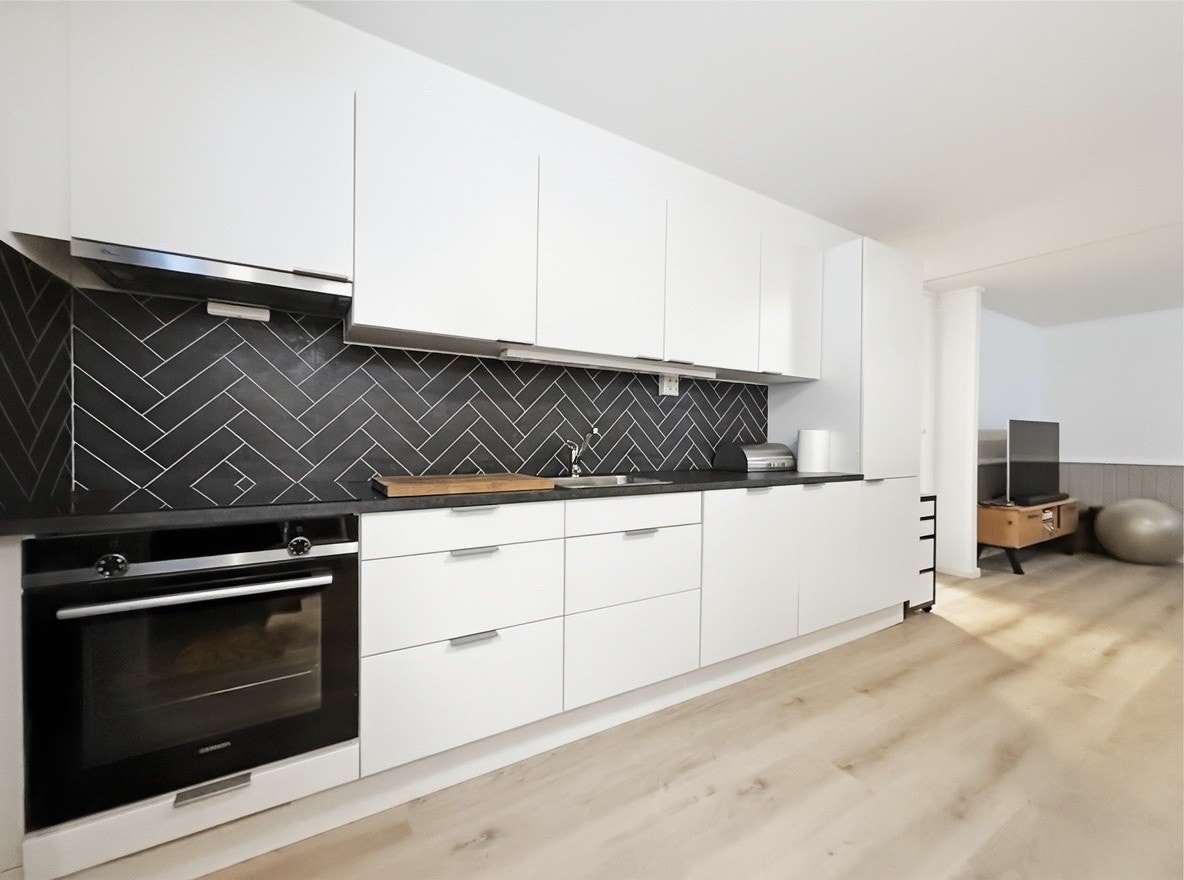 Kjøkken med hvite skap, herringbone vegg, integrert stekeovn og god benkeplass Galleribilde