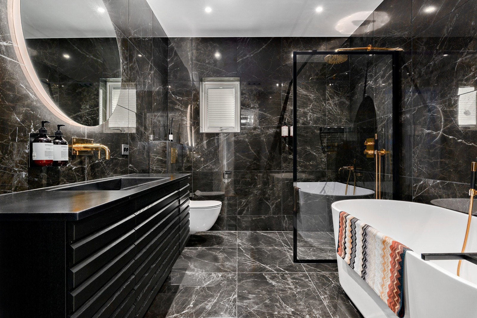 Badet i tilknytning til 1. etasje er stilfullt og tilbyr servant med innredning, speil med sminkelys, stor dusjnisje, vegghengt toalett og badekar. Galleribilde