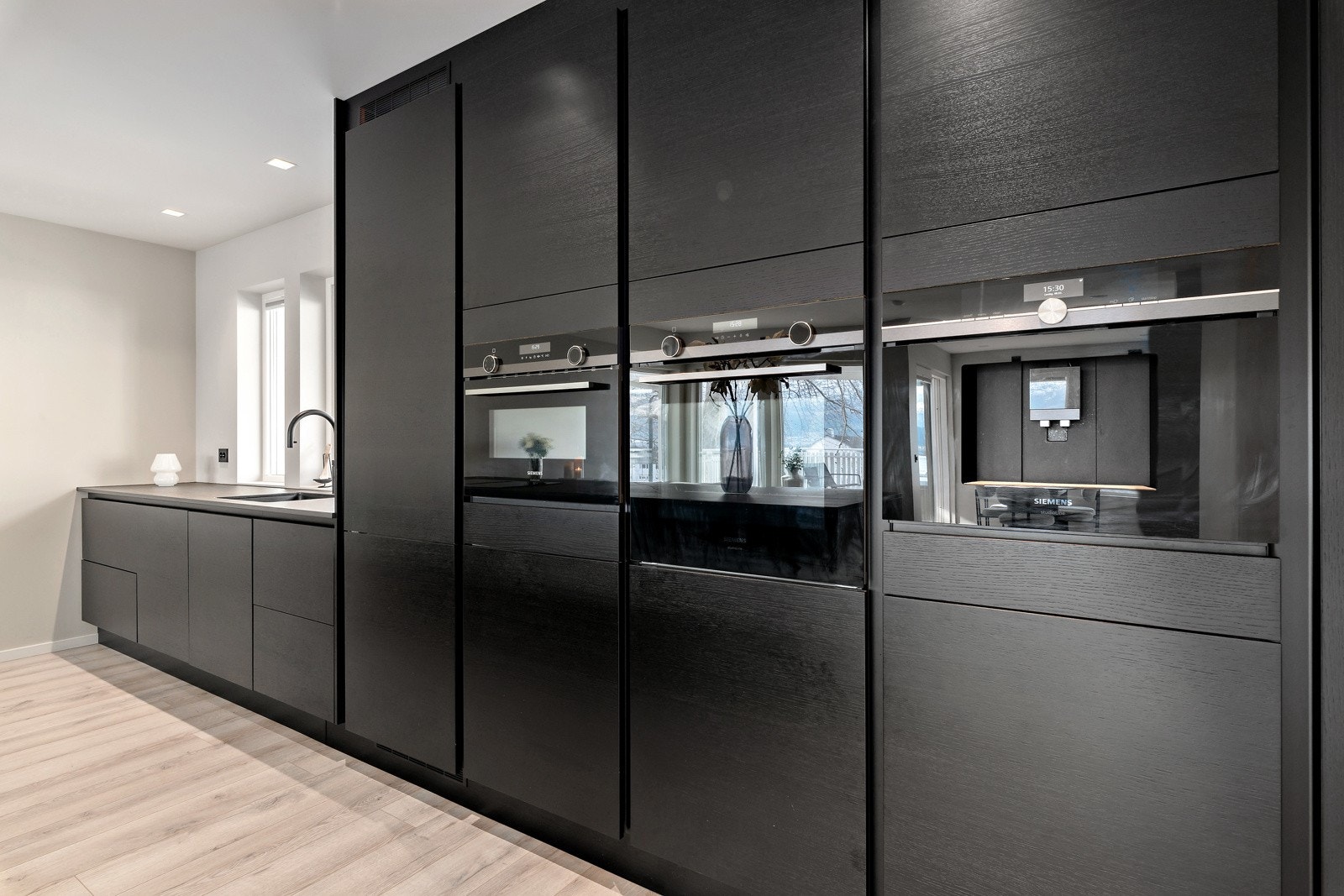 Takhøye skap langs ene veggen med integrert stekeovn, kombiovn, kjøl-/fryseskap, oppvaskmaskin og kaffemaskin. Galleribilde