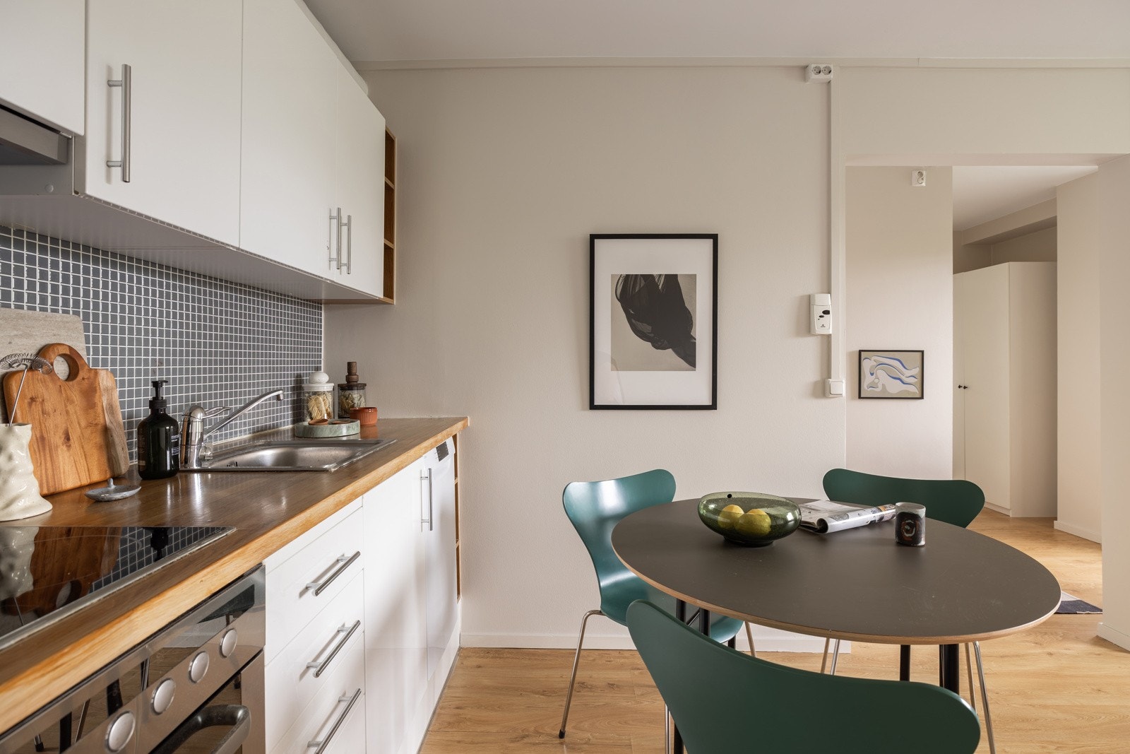 Innredningen har hvite glatte fronter og heltre benkeplate med nedfelt oppvaskkum. Både fint og praktisk med mosaikkfliser i benkeryggen. I enden er det åpne hyller i treverk som gir et pent uttrykk. Galleribilde