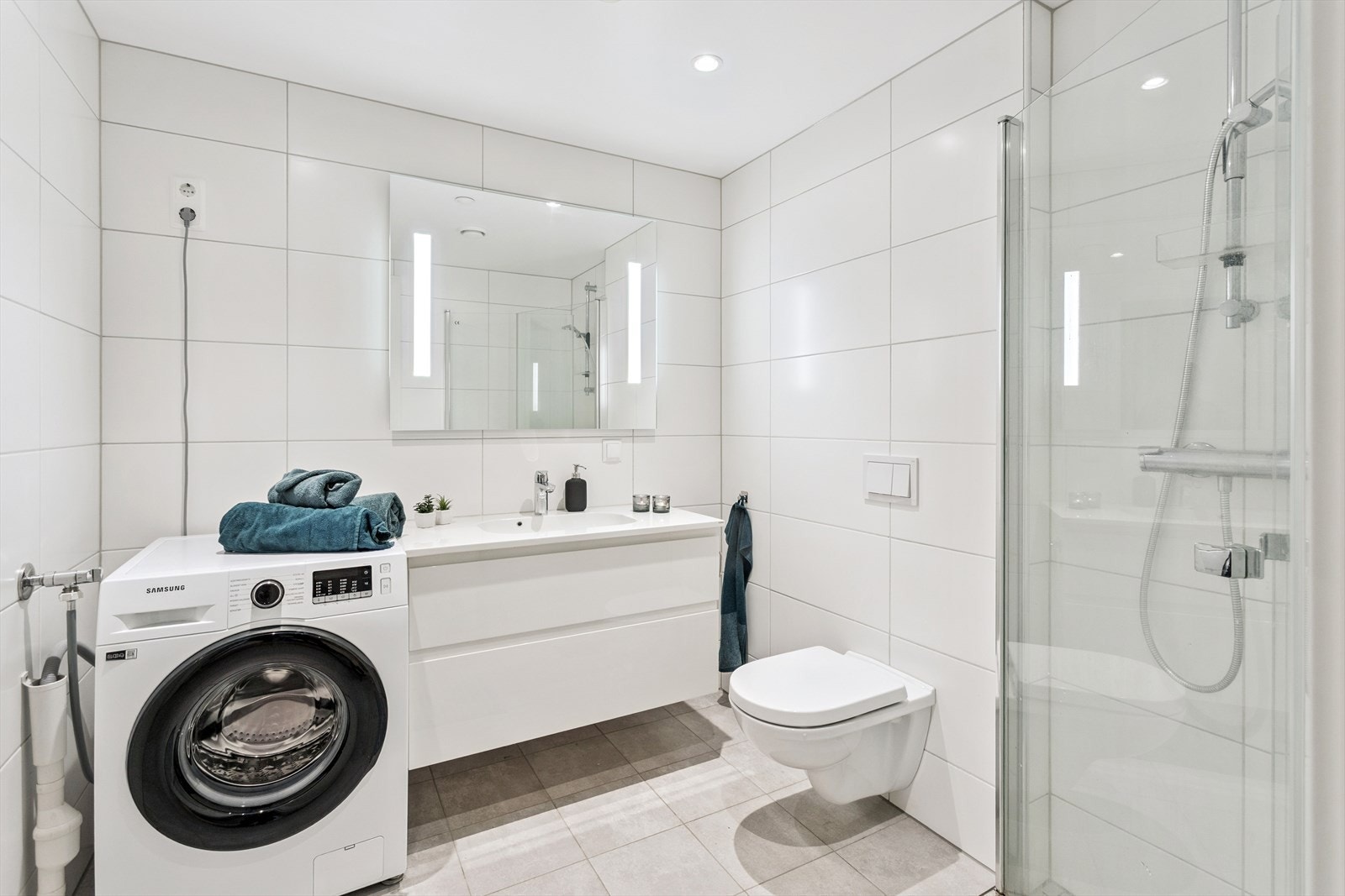 Badet er helfliset og utstyrt med vegghengt toalett, dusjhjørne og opplegg for vaskemaskin. Galleribilde