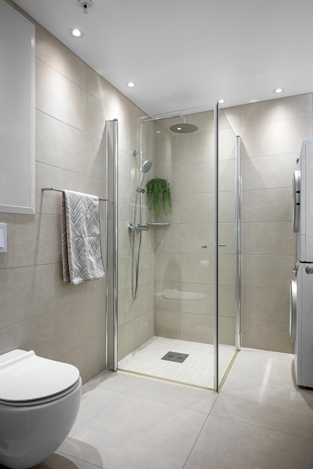 Badet er utstyrt med nedfelt servant, veggmontert toalett, praktiske dusjdører og opplegg for vaskemaskin Galleribilde