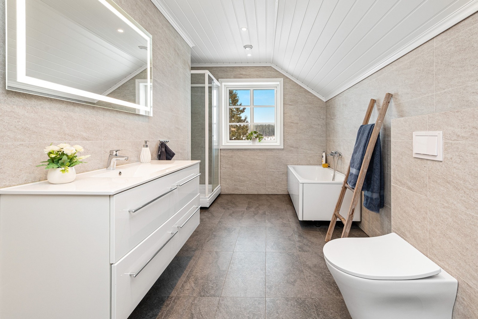 Hvit glatt baderomsinnredning med skuffer og heldekkende vask. Badekar. Speil med lys. Galleribilde