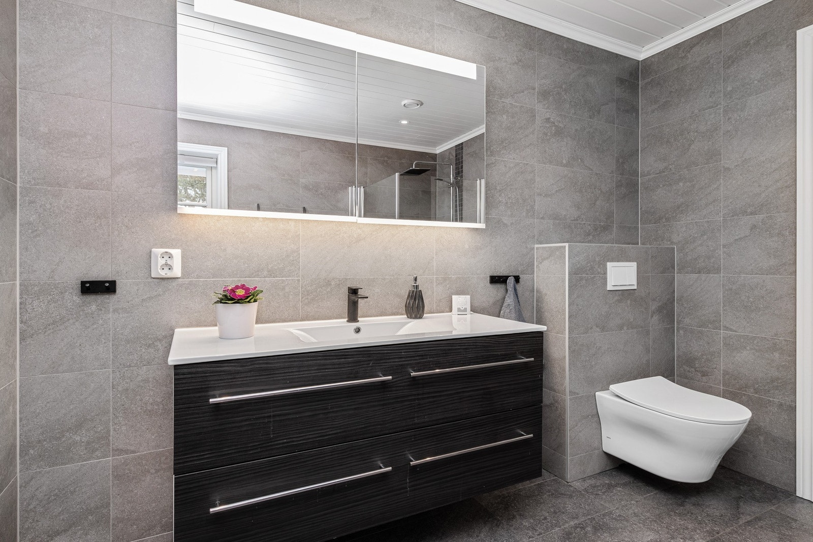 Baderomsinnredning med eikefargede fronter. Heldekkende servant og speil med belysning Galleribilde