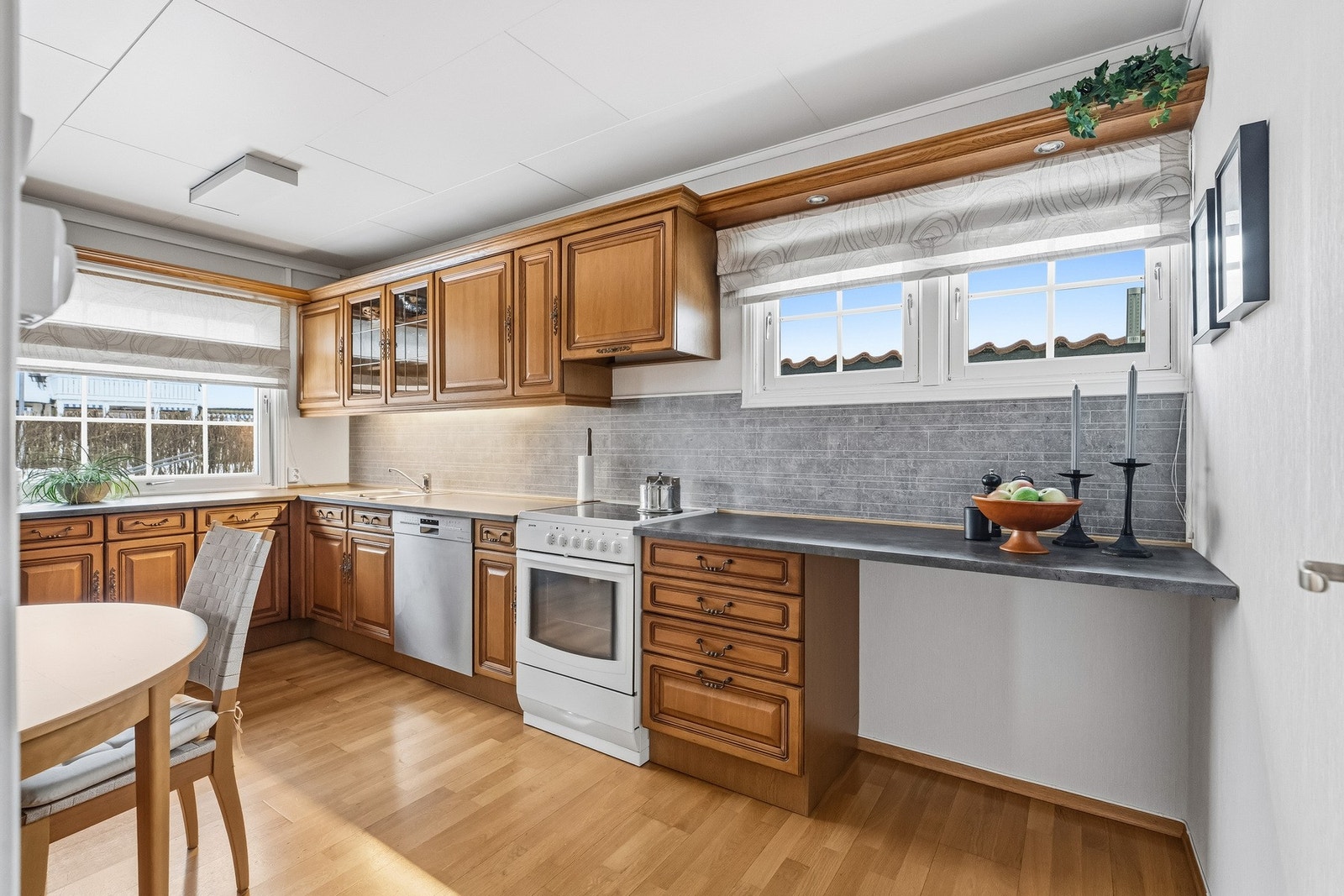 Innredningen har profilerte fronter kombinert med vitrineskap og laminert benkeplate med nedfelt vaskekum i rustfritt stål. Mellom over- og underskap er det montert flisimiterte kitchenboards, samt integrert belysning. Galleribilde