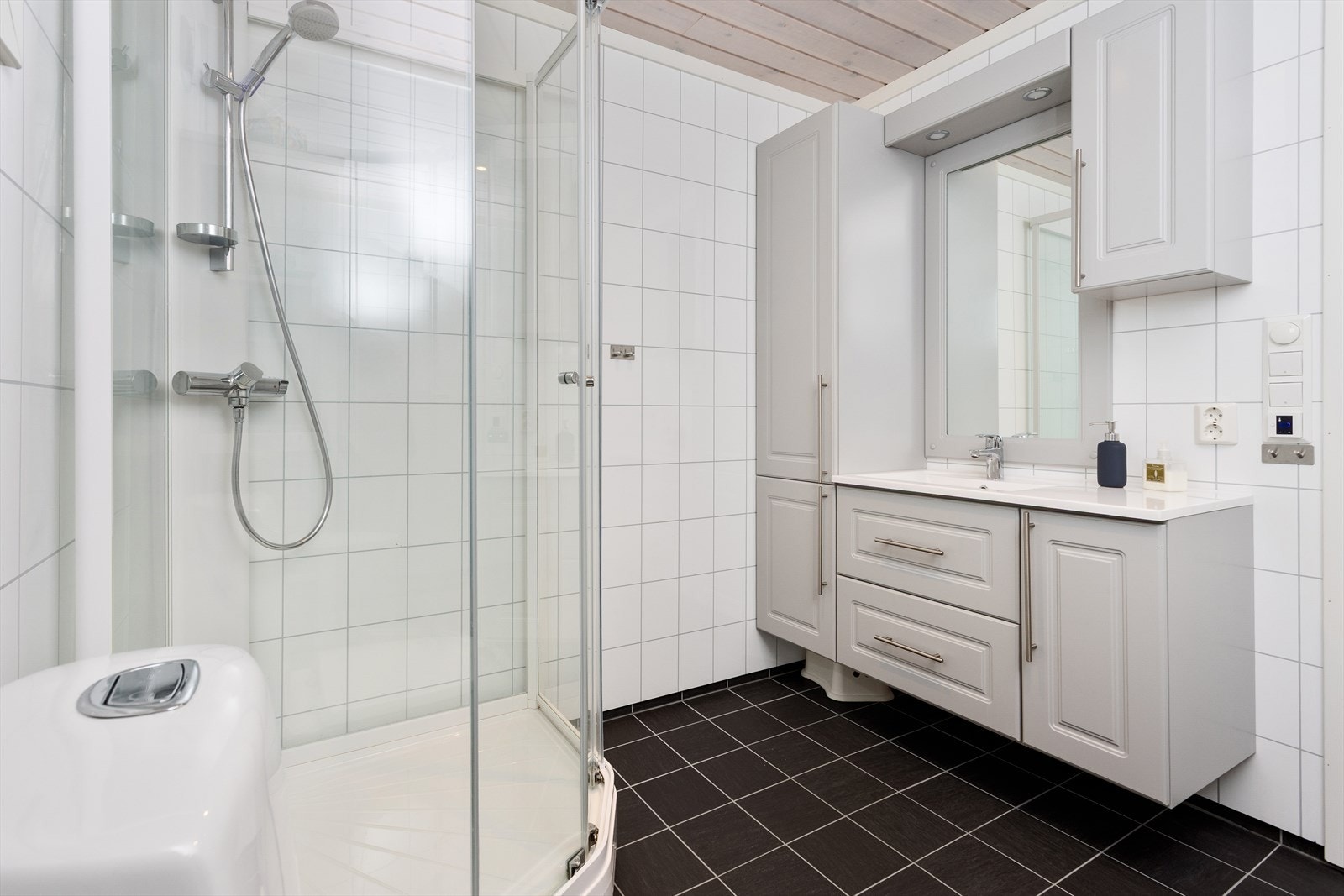 Badet er lyst og tidløst, med baderomsplater på veggene og panel i taket. Gulvet er flislagt og utstyrt med elektriske varmekabler for ekstra komfort. Galleribilde