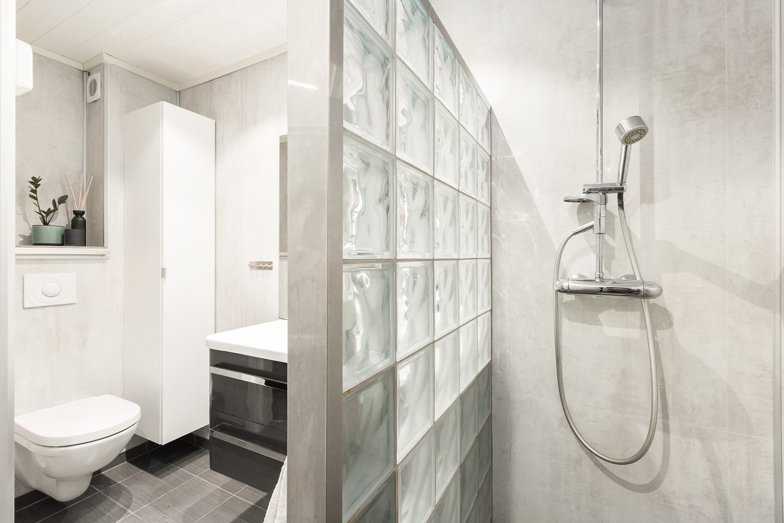 Rommet har baderomsplater på vegger, flislagt gulv med varmekabler og elektrisk styrt vifte. Galleribilde