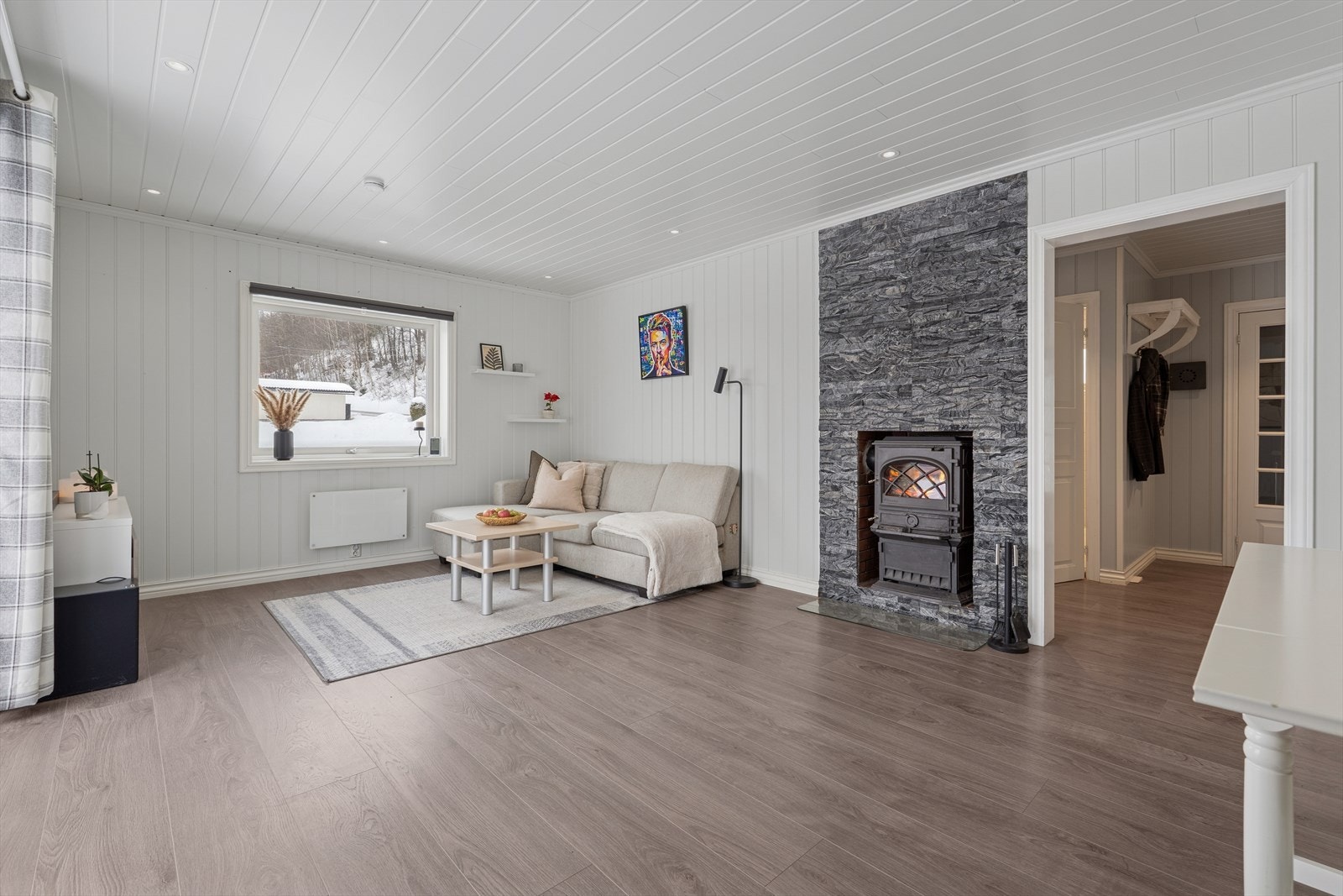 Stuen er et lyst og åpent rom med en sentralt plassert vedovn for varme og hygge. Galleribilde