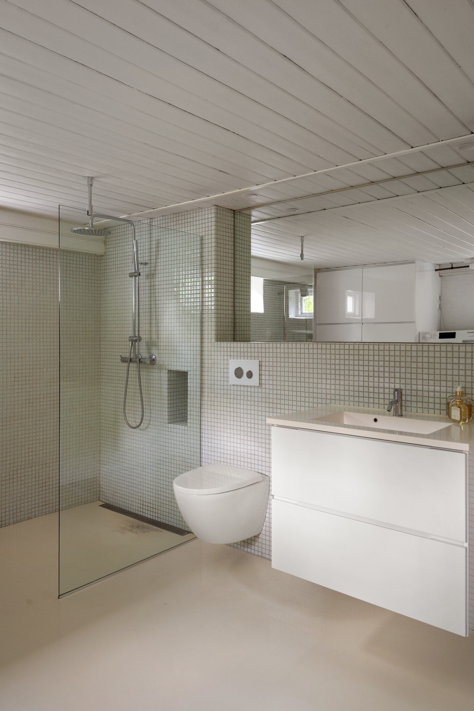 I kjelleretasjen er det et stort, innbydende bad med lyse mosaikkfliser på veggene, lyst gulv og hvit panel i himlingen. Galleribilde