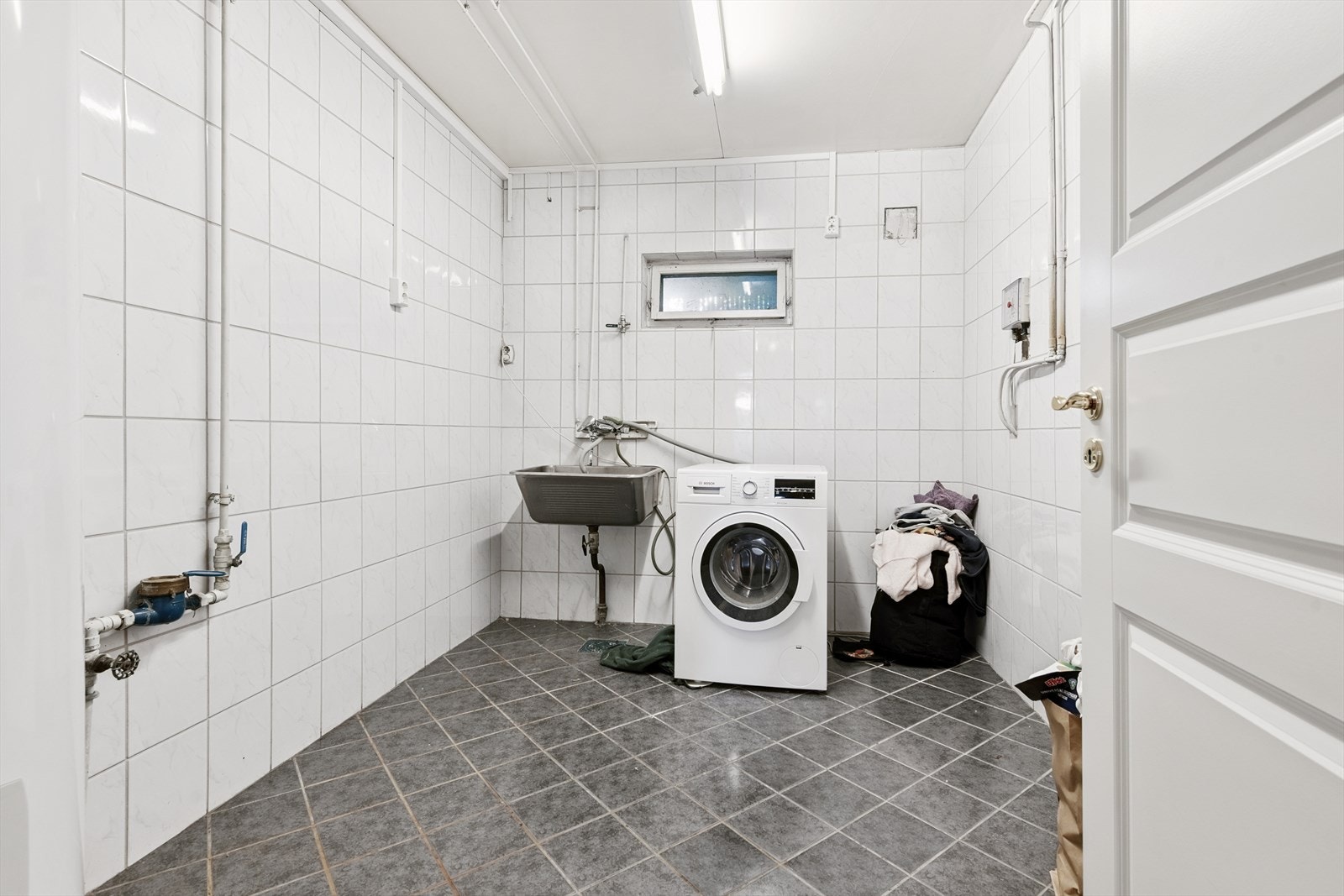 Flislagt vaskerom i underetasje med opplegg for vaskemaskin og skyllekum. Galleribilde