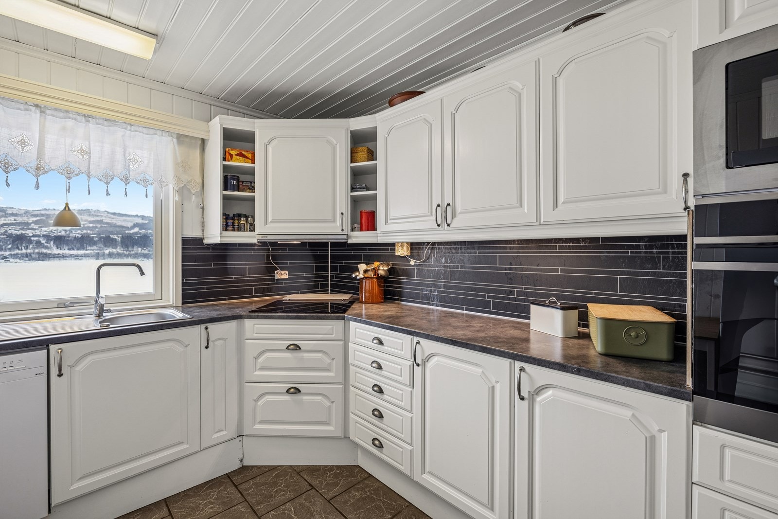 Kjøkkenet har en pen innredning med hvite, profilerte fronter og laminert benkeplate med kjøkkenkum. Galleribilde