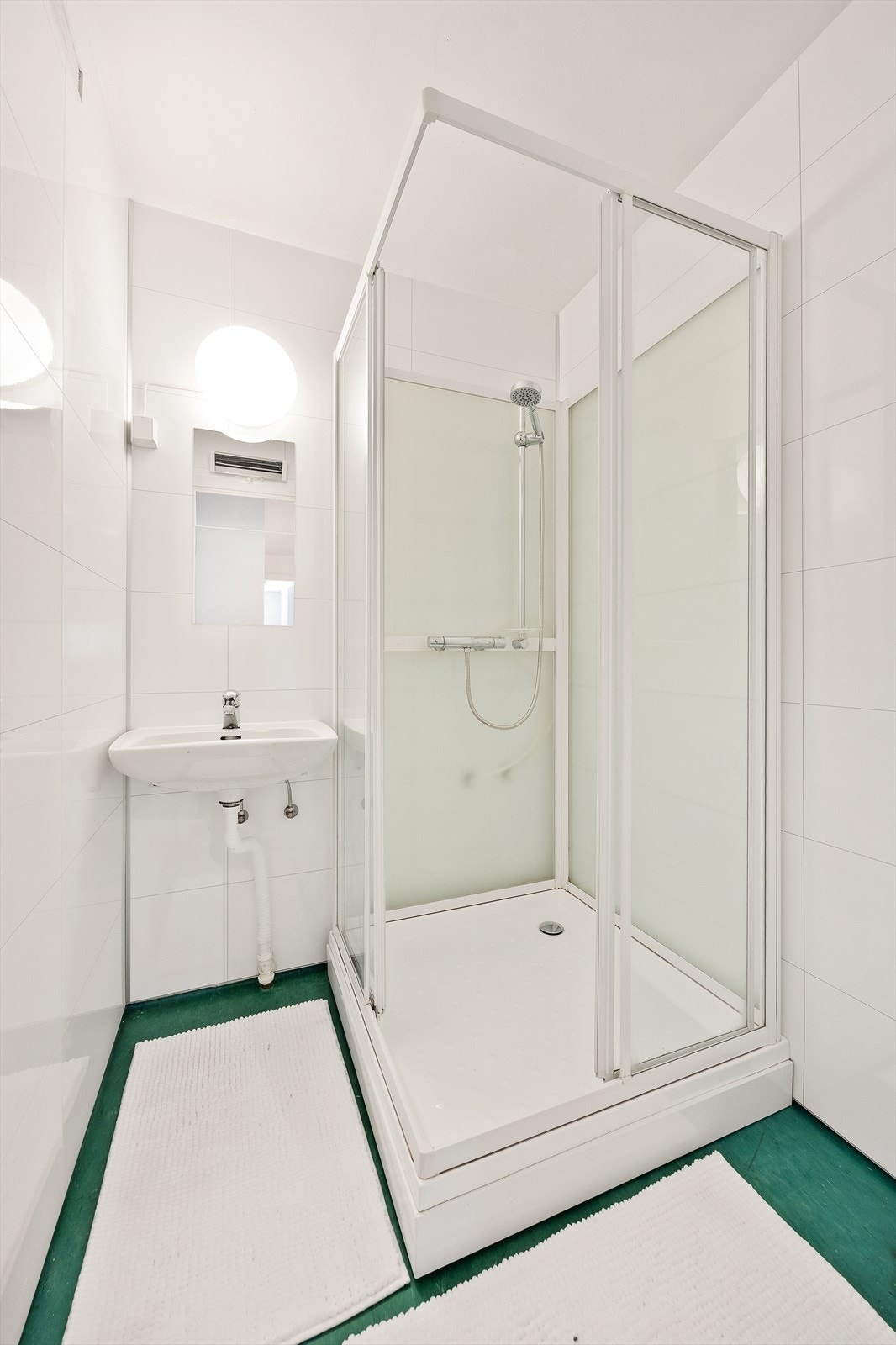 Flislagt bad med servantseksjon, dusjkabinett og veggmontert speil. Galleribilde