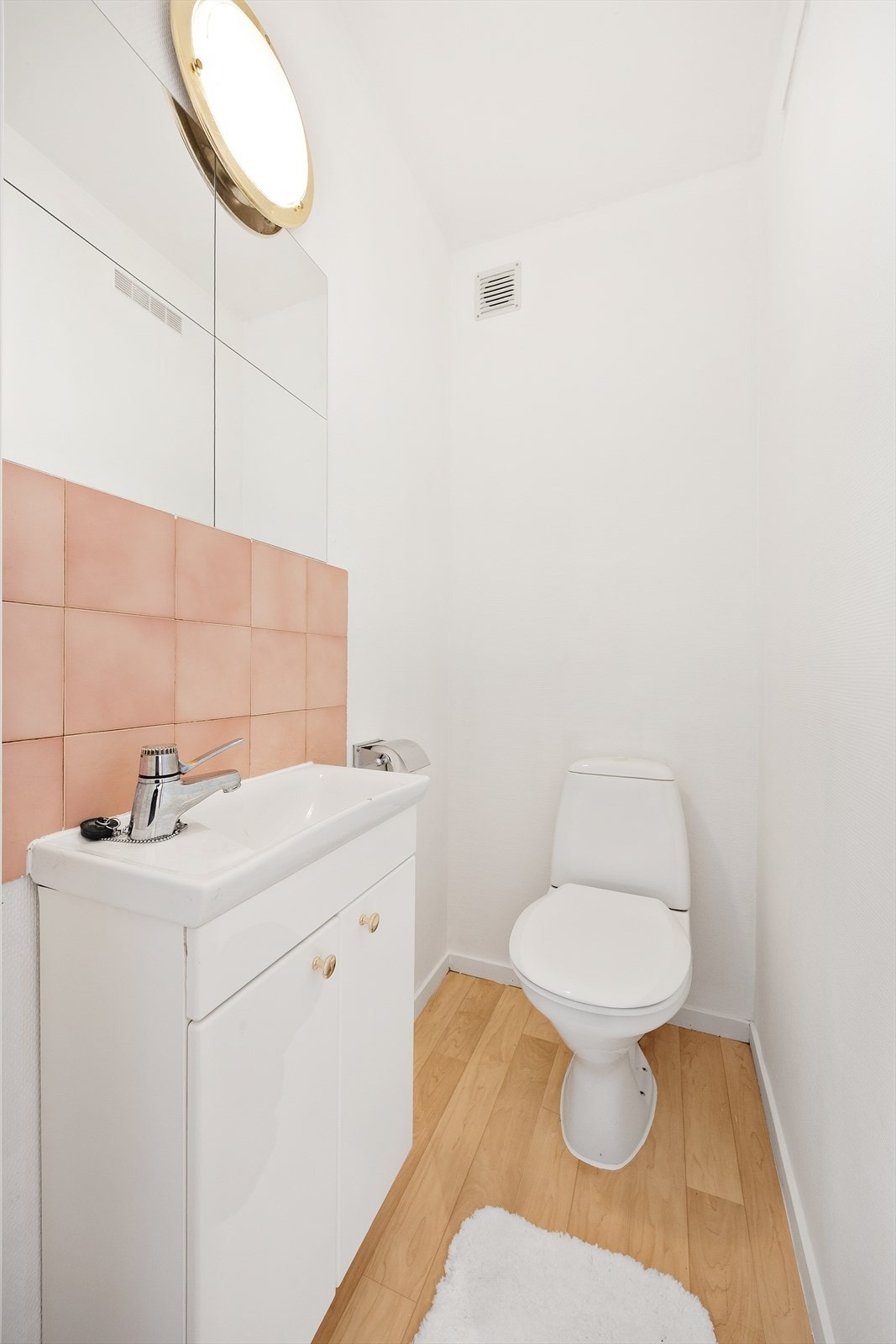 Toalettrom med gulvmontert klosett, servantseksjon med skap og fliser på vegg. Galleribilde