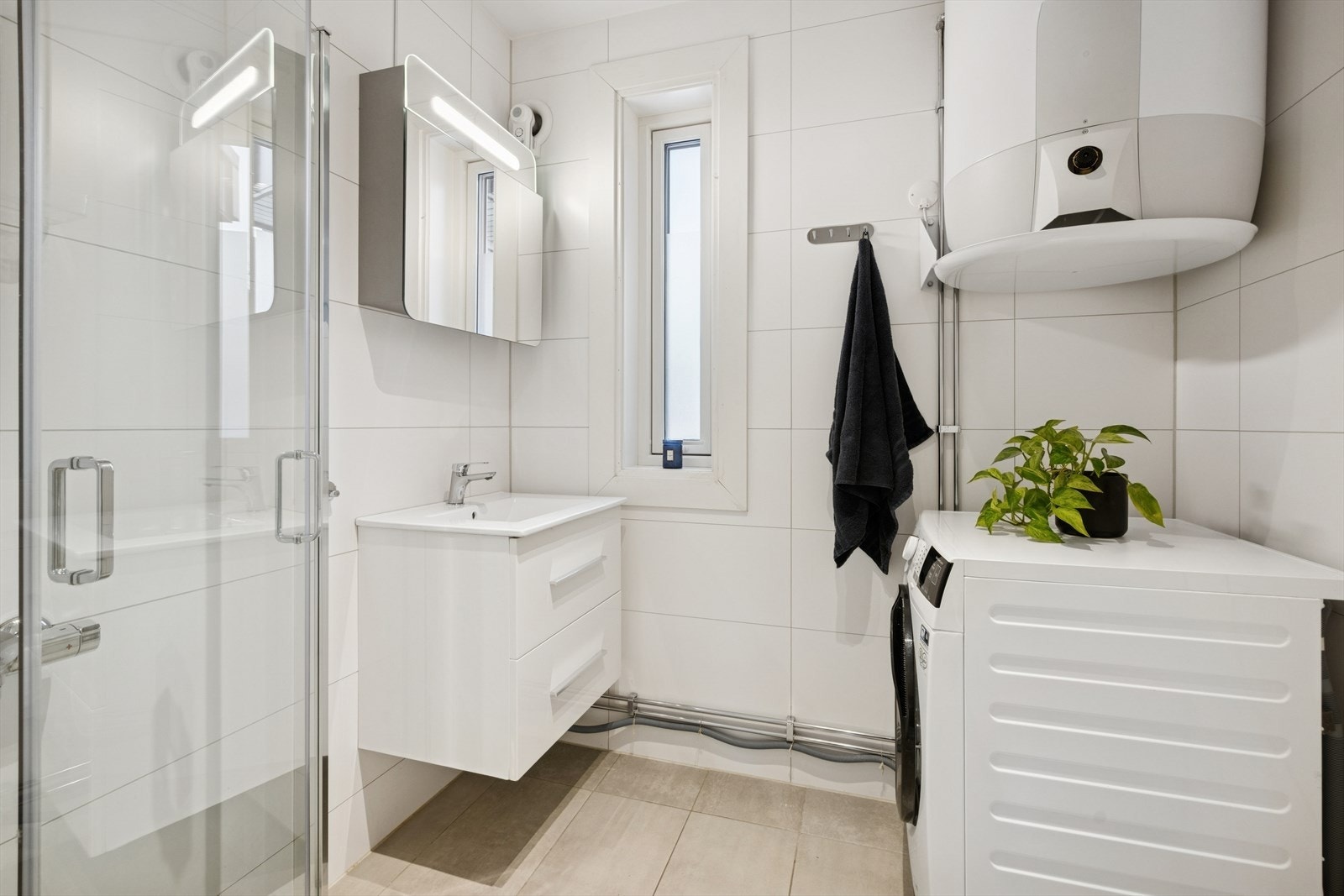 Flislagt baderom med praktisk løsning, utstyrt med servant nedfelt i skapinnredning og dusjhjørne. Opplegg for vaskemaskin. Galleribilde