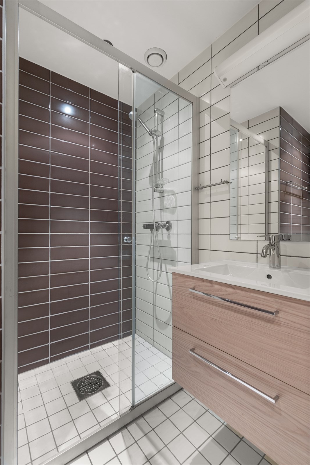 Badet har gulv og veger med fliser og elektrisk gulvvarme. Badet er innredet med klosett, servant med innredning, speil og dusjnisje mer skyvbar glassdør. Mekanisk avtrekk sørger for behagelig inneklima. Galleribilde