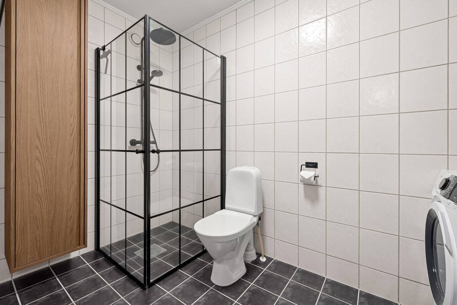 Badet er utstyrt med toalett, toppmontert servant, dusjhjørne med glassvegger, veggskap og opplegg for vaskemaskin. Galleribilde