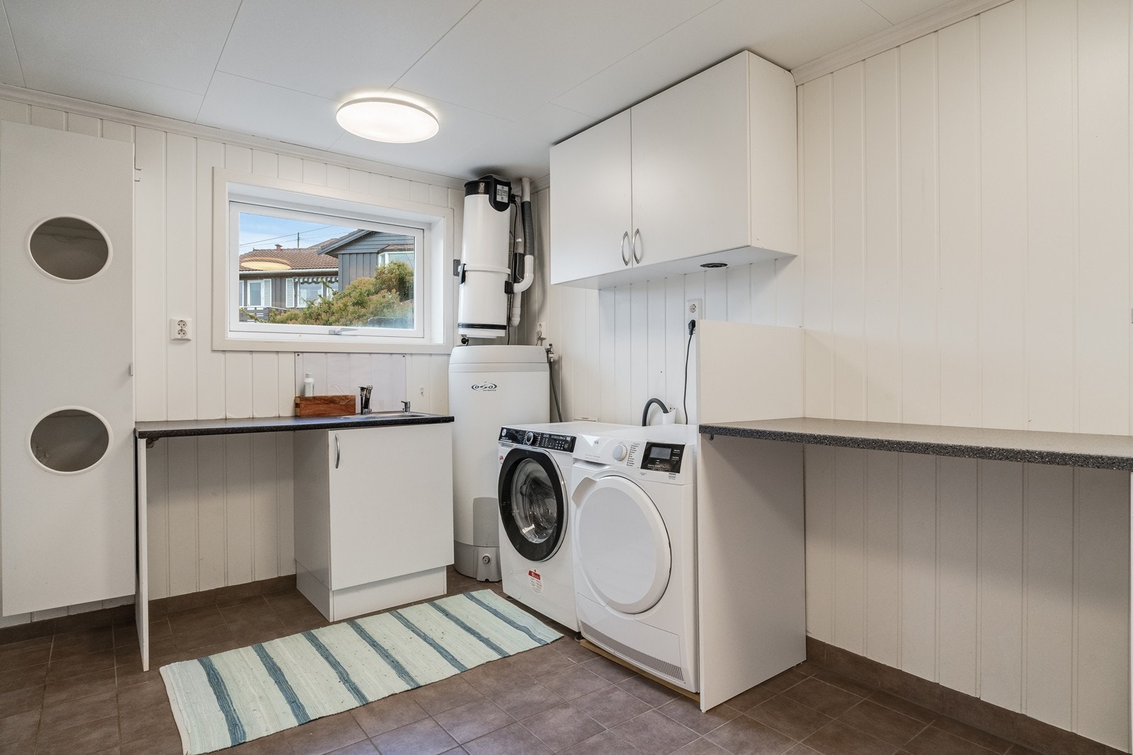 Et praktisk og funksjonelt vaskerom med innredning bestående av skap og benker som gir gode arbeidsforhold og oppbevaringsmuligheter (deler av vaskerom ikke godkjent ref pkt. ferdigattest). Galleribilde