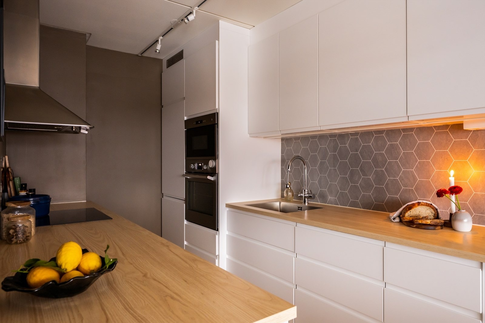 Innredning med glatte, fabrikklakkerte fronter og laminatbenkeplate med planlimt kum i rustfritt stål. Stålplate bak platetopp og belysning under overskap gir både funksjon og et stilrent preg. Galleribilde